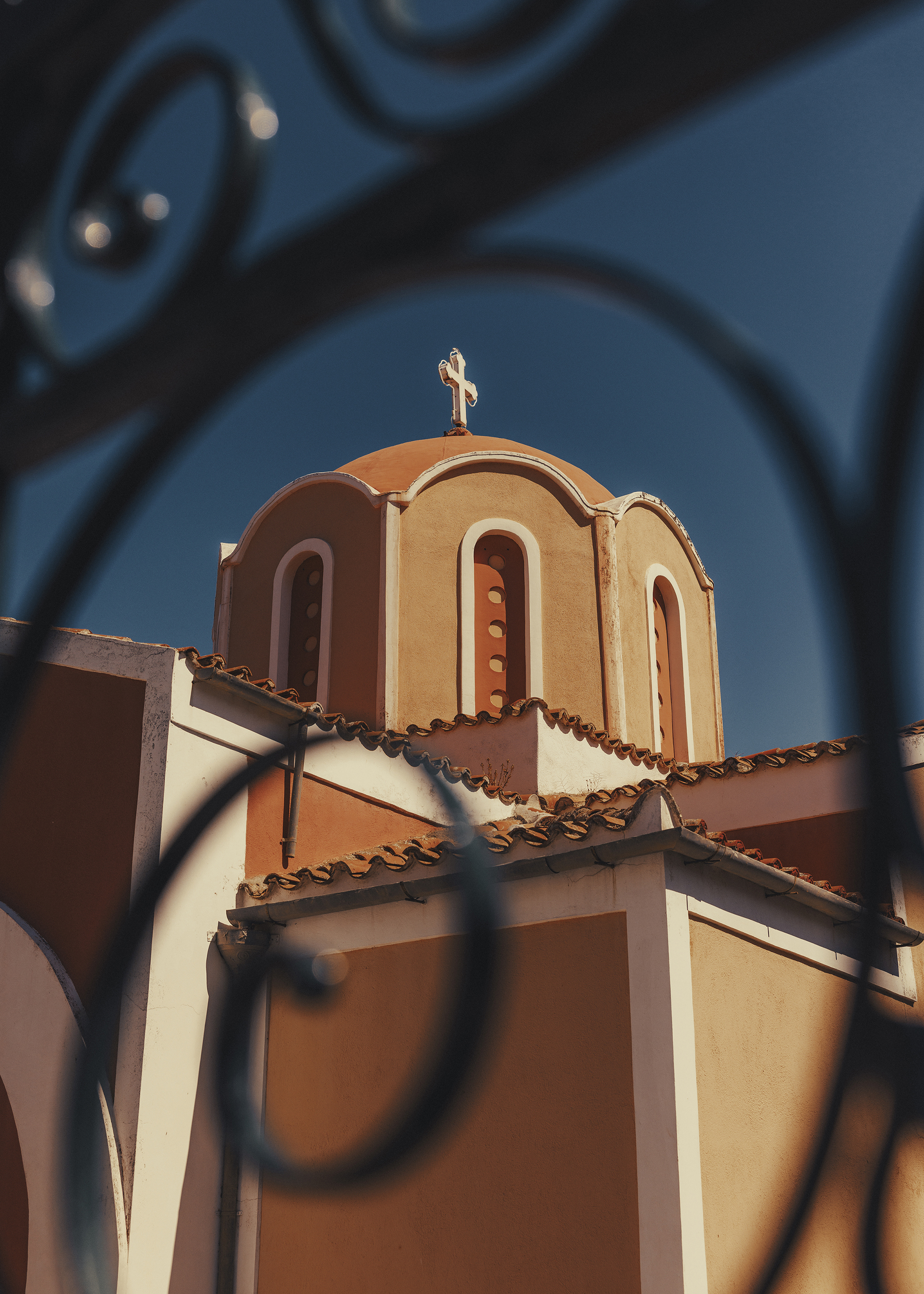 Orange and white dome of a church with a cross at its peak shot through a curved black steel gate