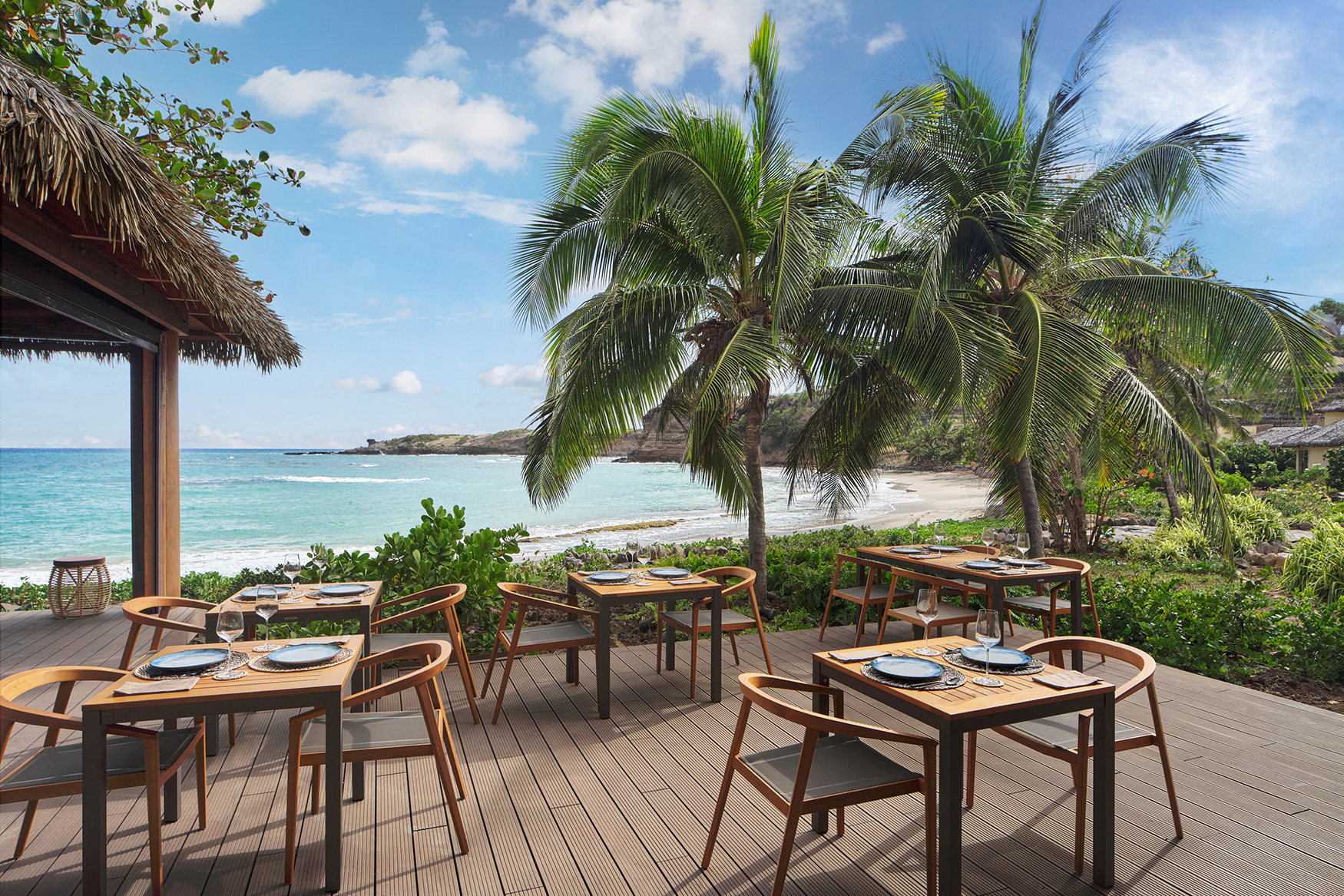 Wooden tables surrounded by palm trees and the shore line at Seafire Restaurant