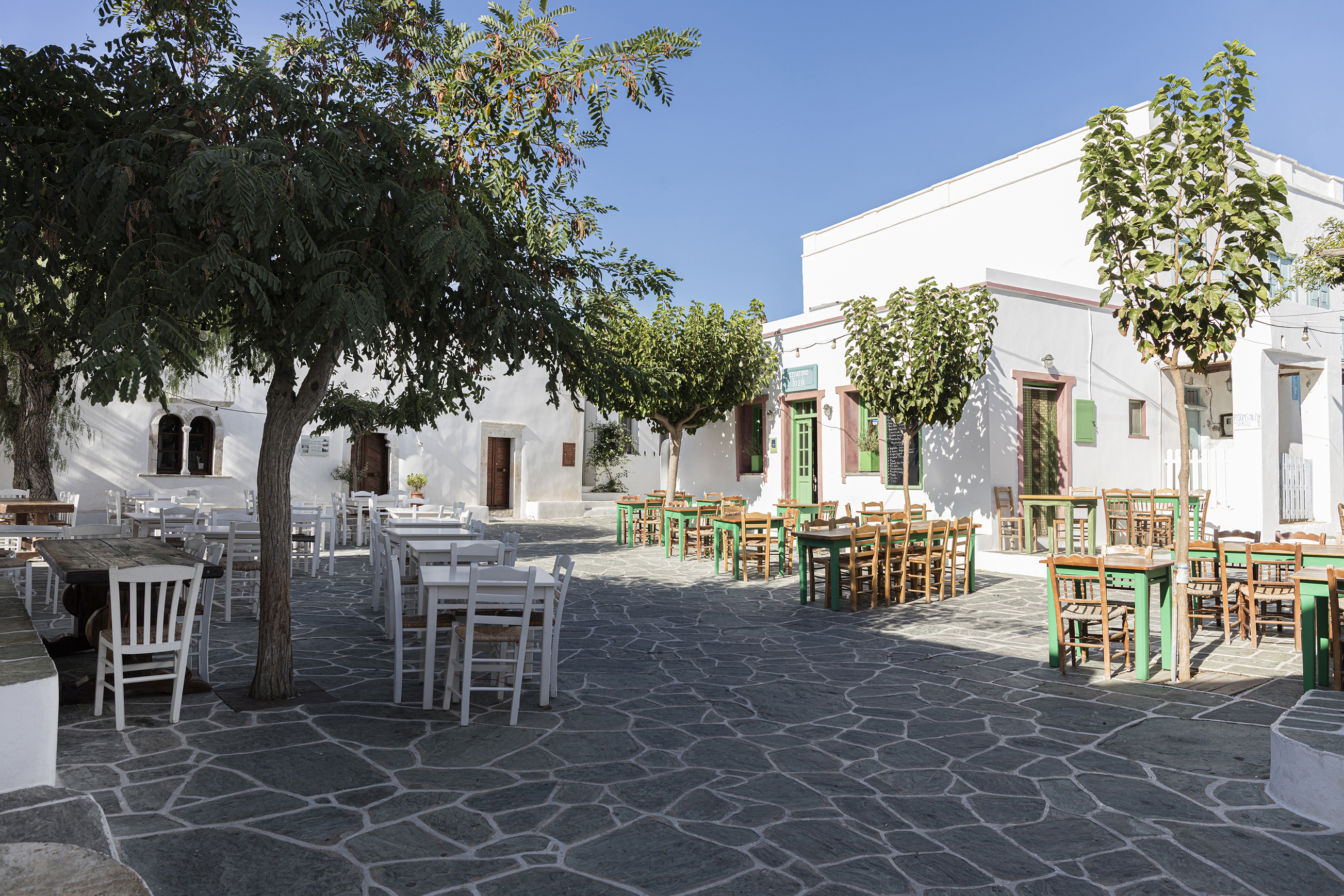 Cobbled square half shaded and dotted with trees and wooden dining tables 