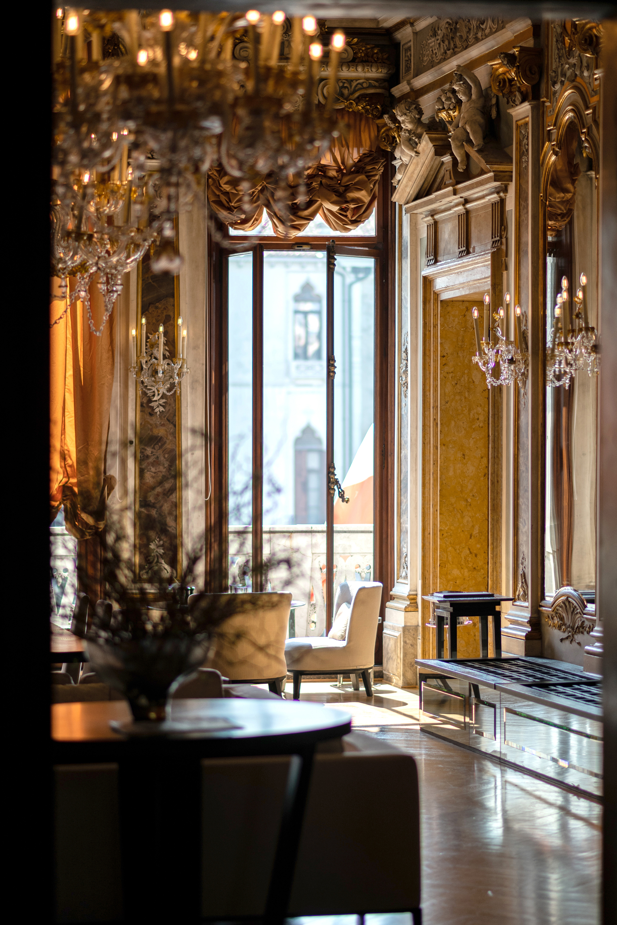 The details of a lavish room including ornate wall sculpting, sconces and large window 