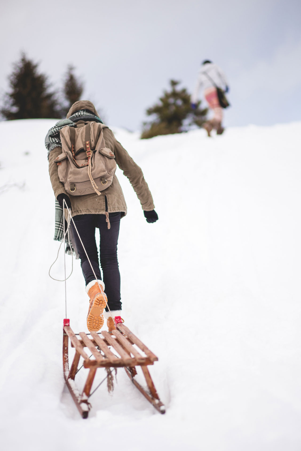 A person pulling a wooden sled behind them up a small hill