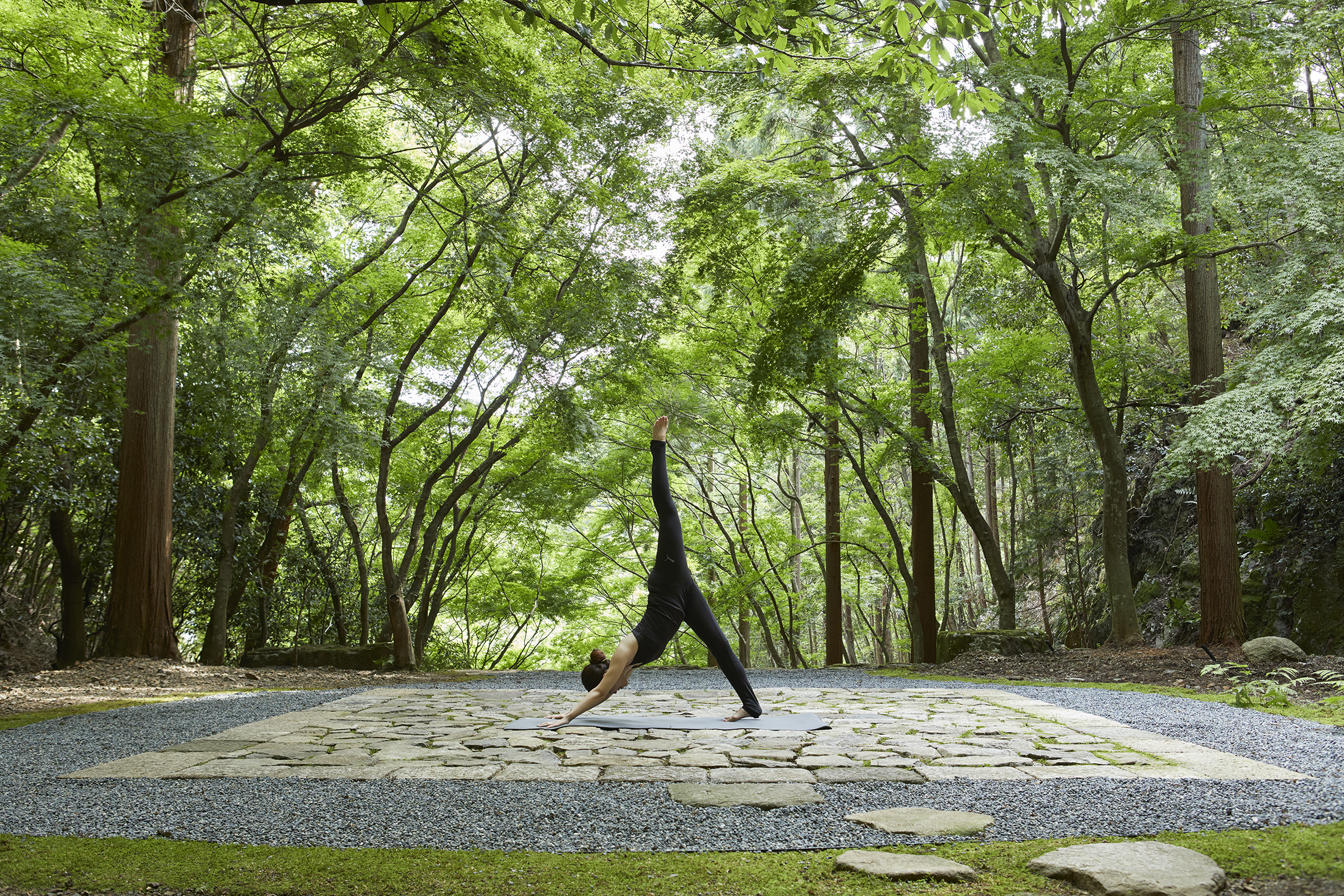 A woman practicing yoga on a stone patio in the Temgamine Garden beneath green trees
