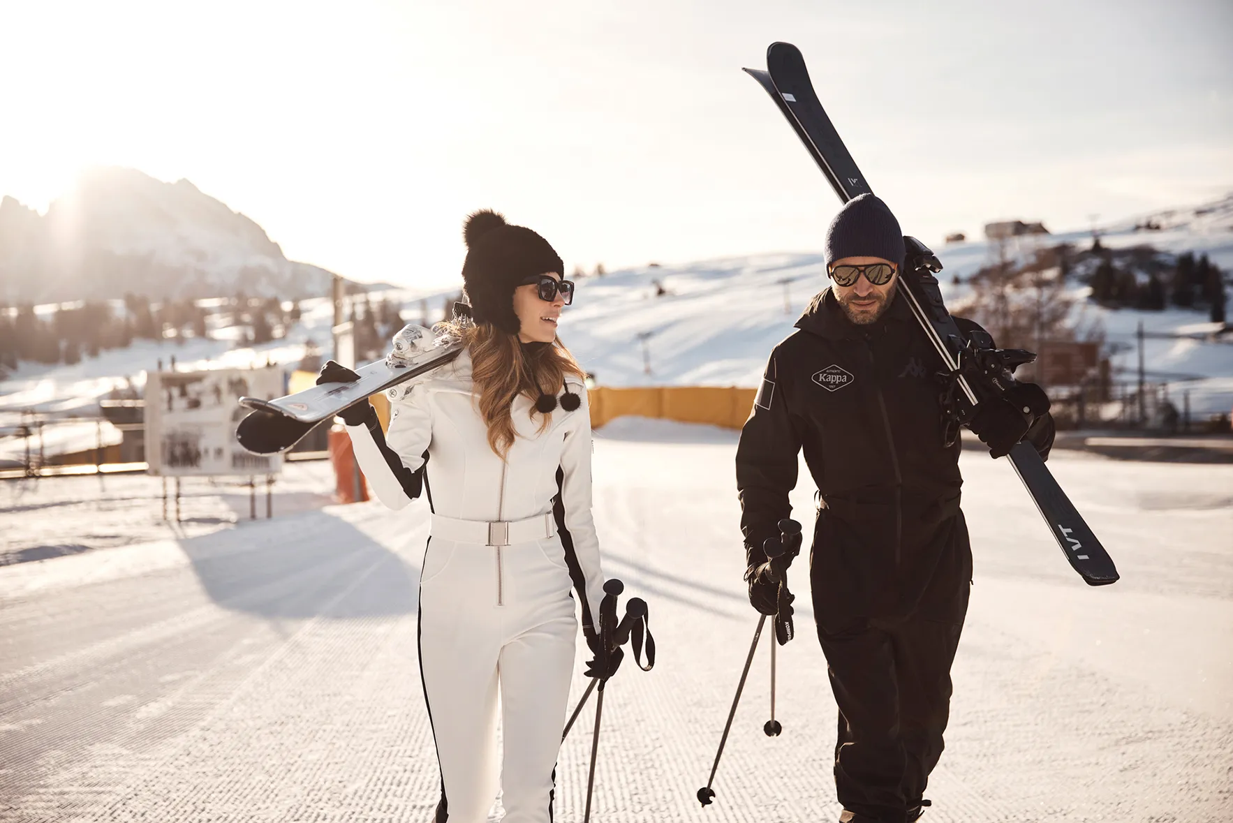 A couple walking together holding skis 
