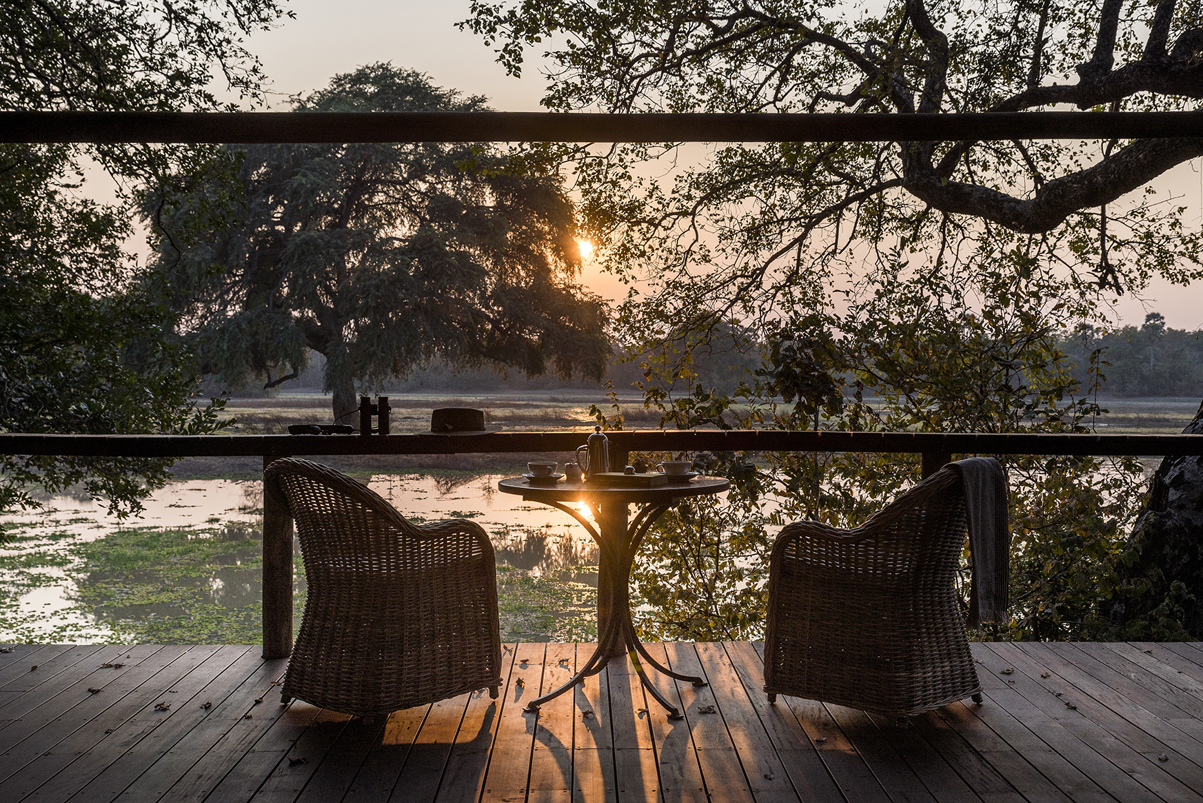 Africa, Zambia, Sungani Lodge, two wicker chairs and a table on a private deck at sunset
