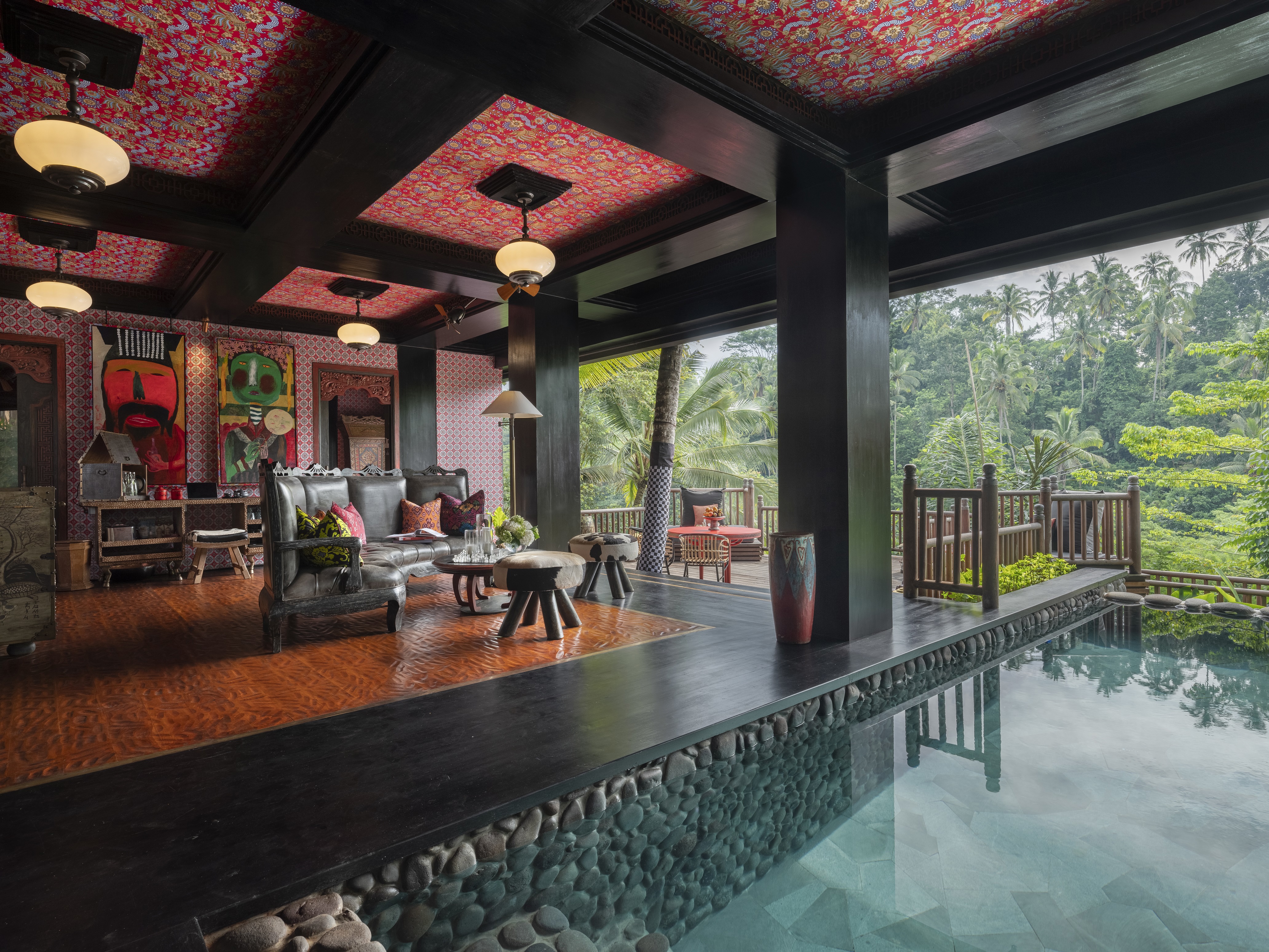 An large ornate lounge featuring accents of red and dark wood with an indoor outdoor pebbled swimming pool at Capella Ubud