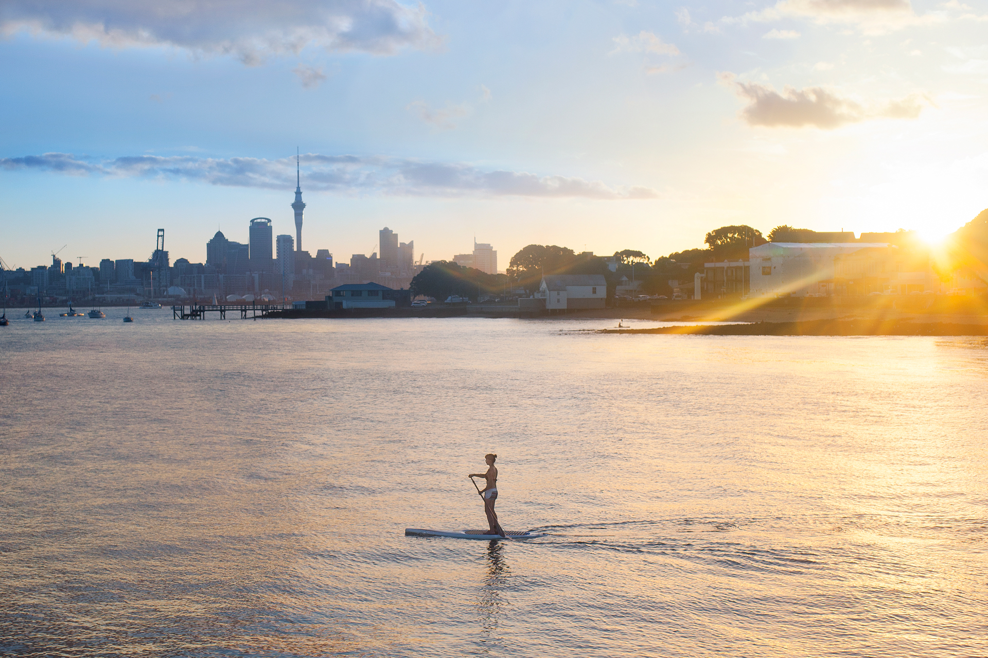 A person paddle boarding on water with Auckland City in the background 