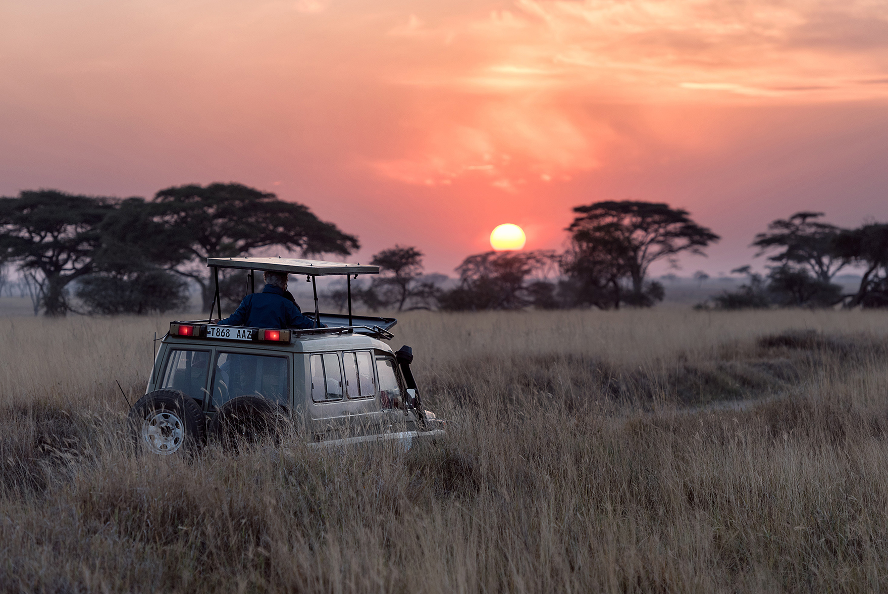 Game Drive jeep stopped facing the sunset in African grasslands