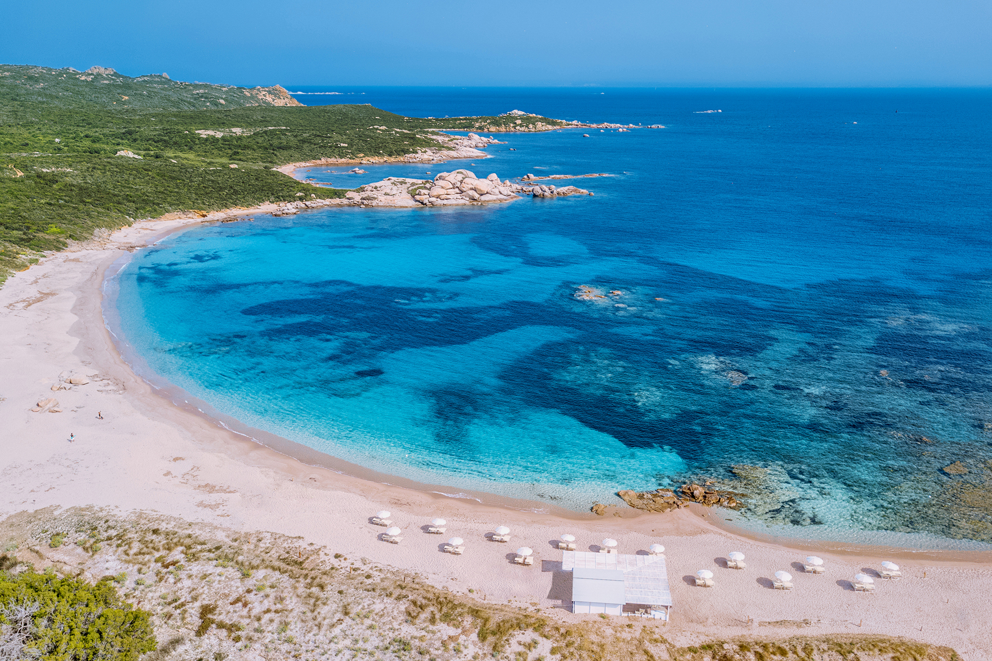 A small bay featuring a white bar and sun loungers on the beach at Valle Dell'Erica