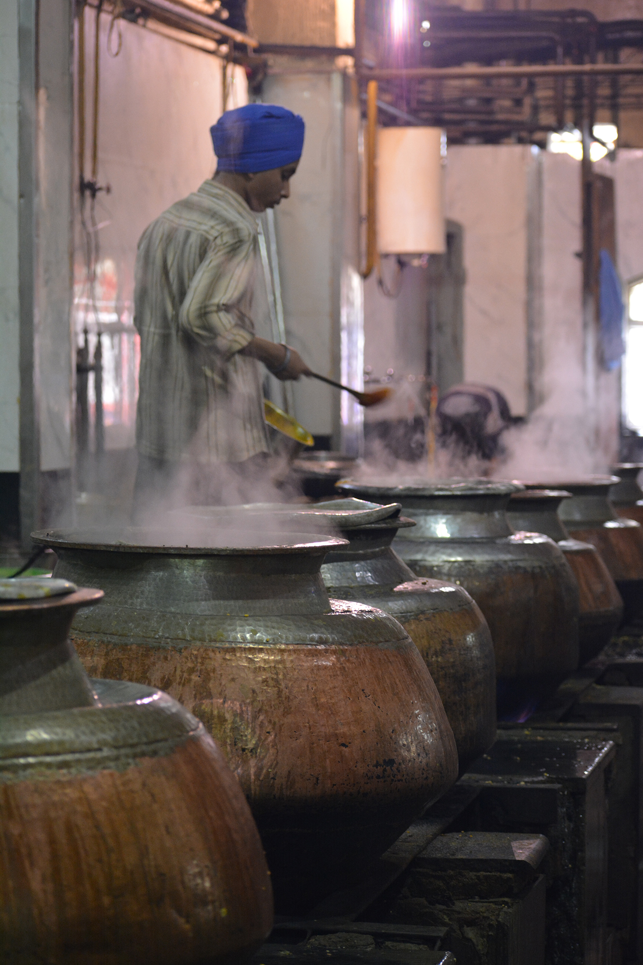 A line of large cooking pots with a man behind looking into them
