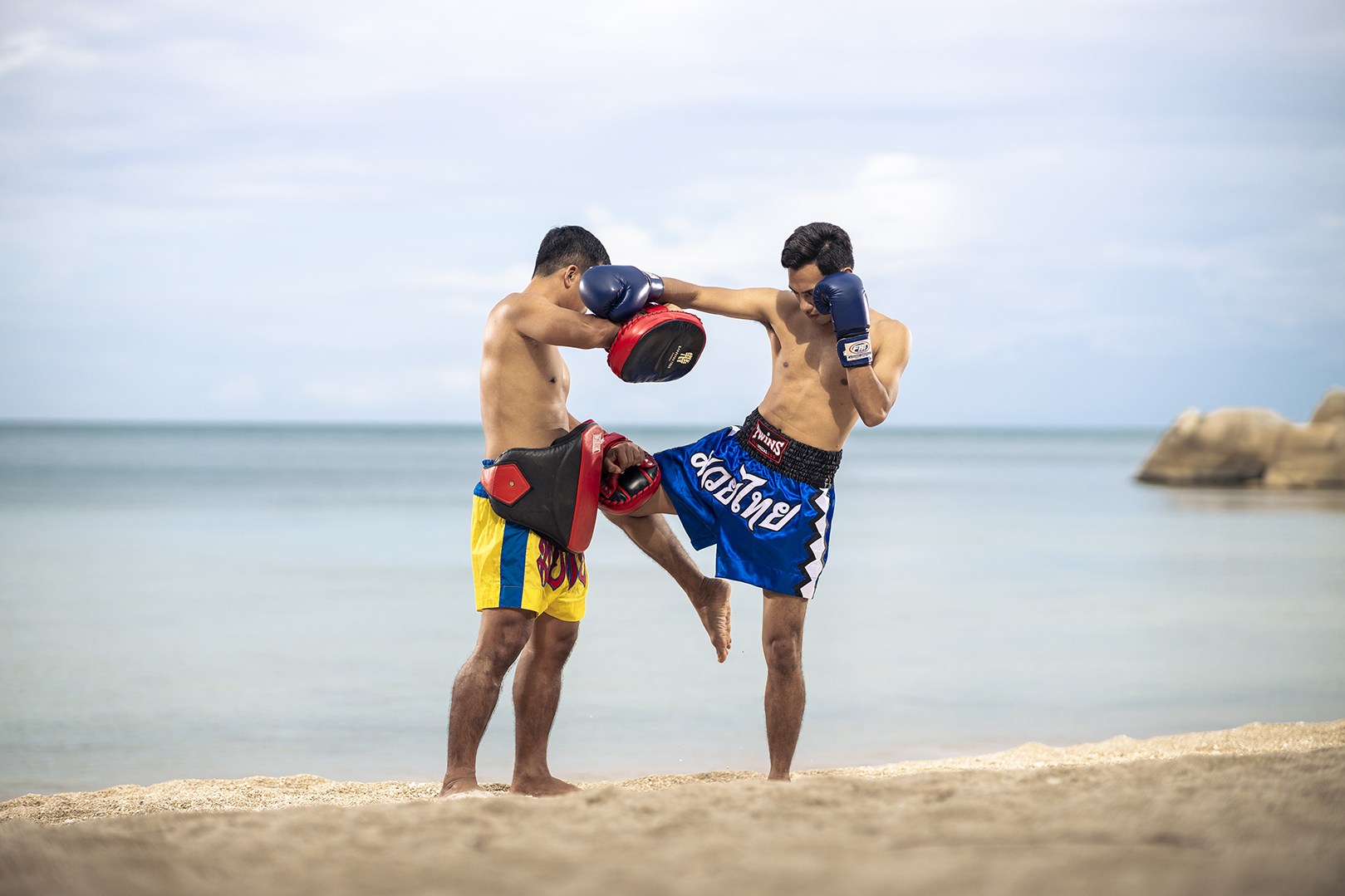 Two men in traditional attire practicing muay thai on the beach in Koh Samui
