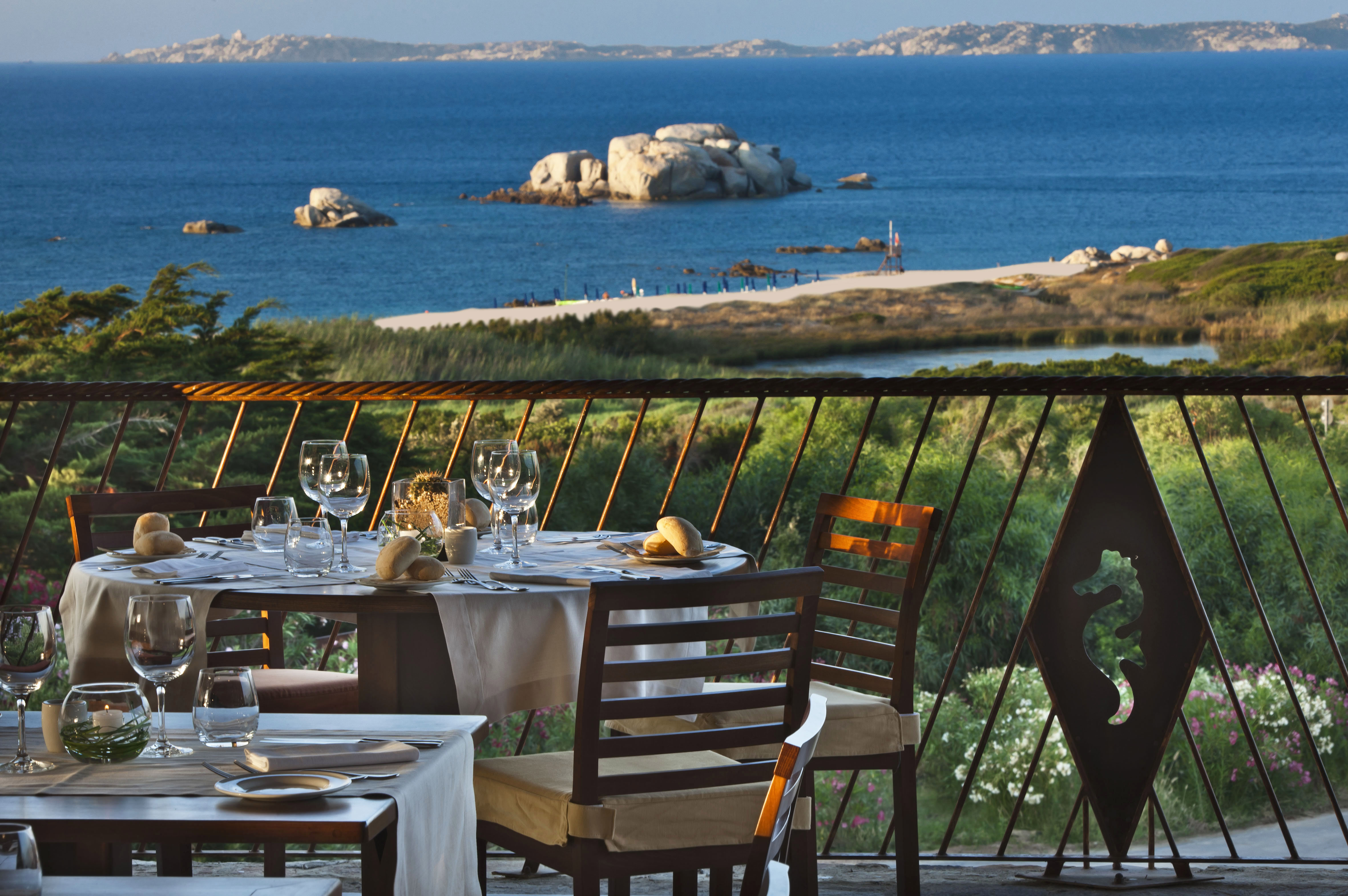 Two tables set for dinner on an outdoor terrace overlooking a beach and ocean