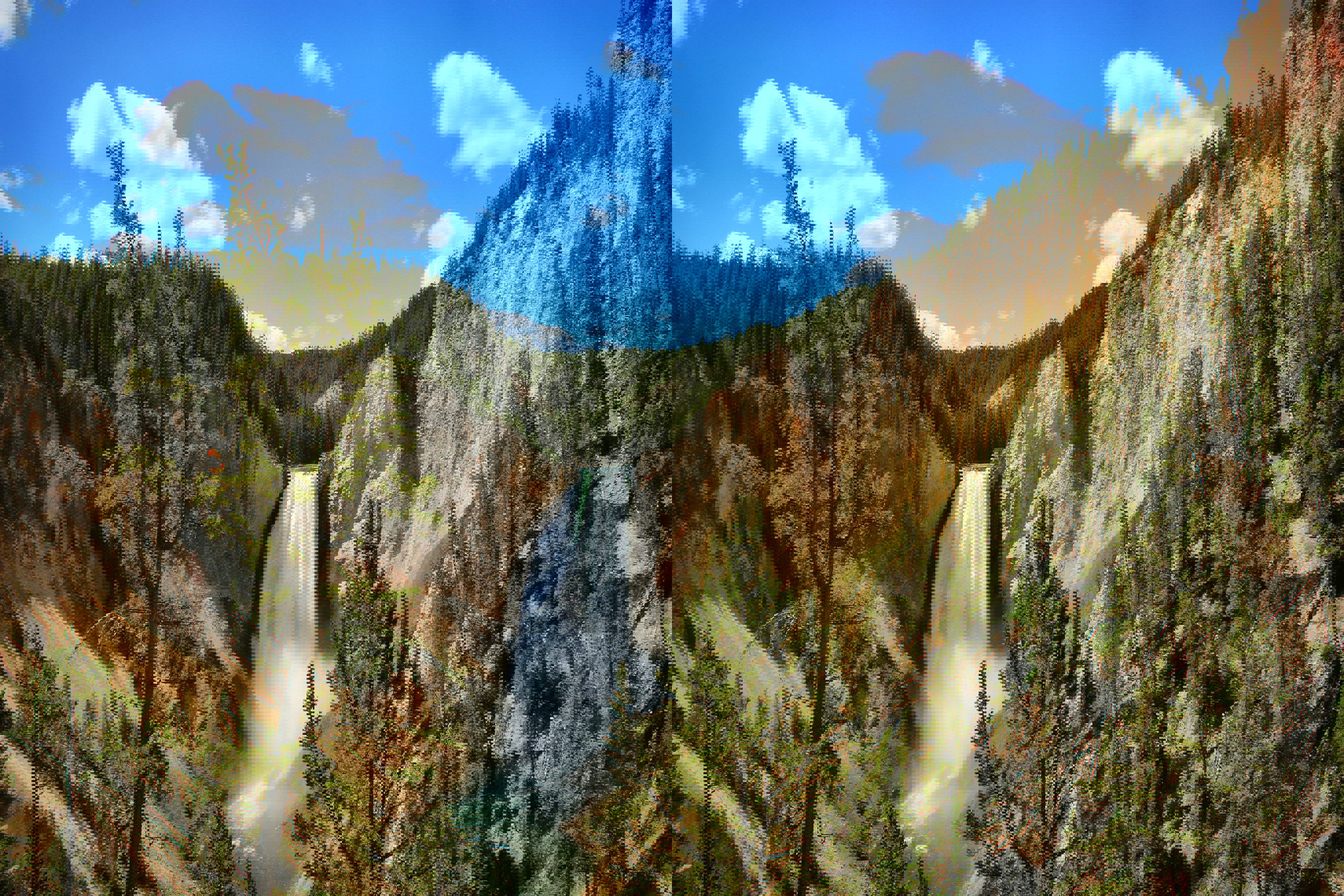 A waterfall surrounded by trees beneath a clear blue sky dotted with white clouds