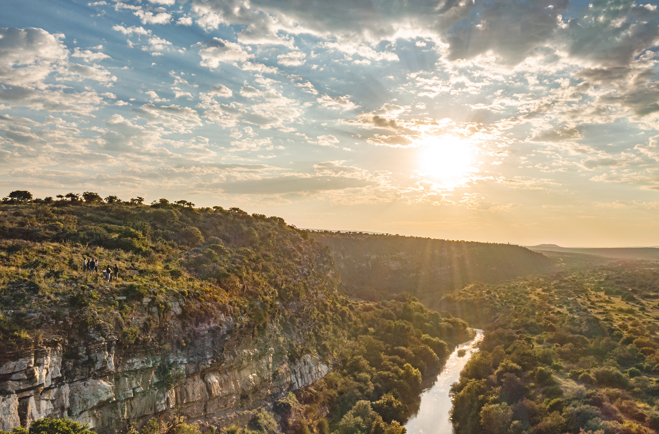 Green valley landscape cut through by a river with people standing on a cliff to the left