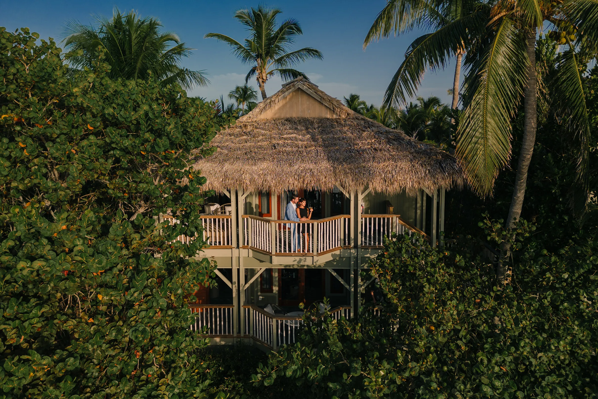 Thatched-roof luxury bungalow surrounded by lush palm trees at Little Palm Island Resort in Florida Keys.