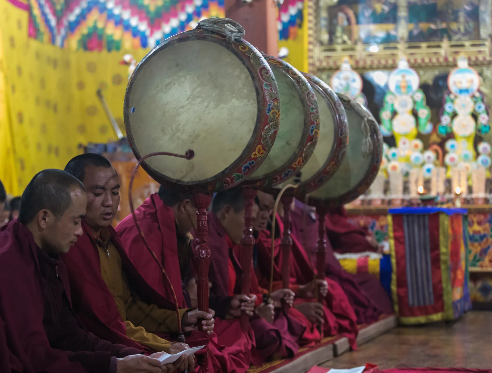 Monks seated in a temple playing large drums during a traditional ceremony.