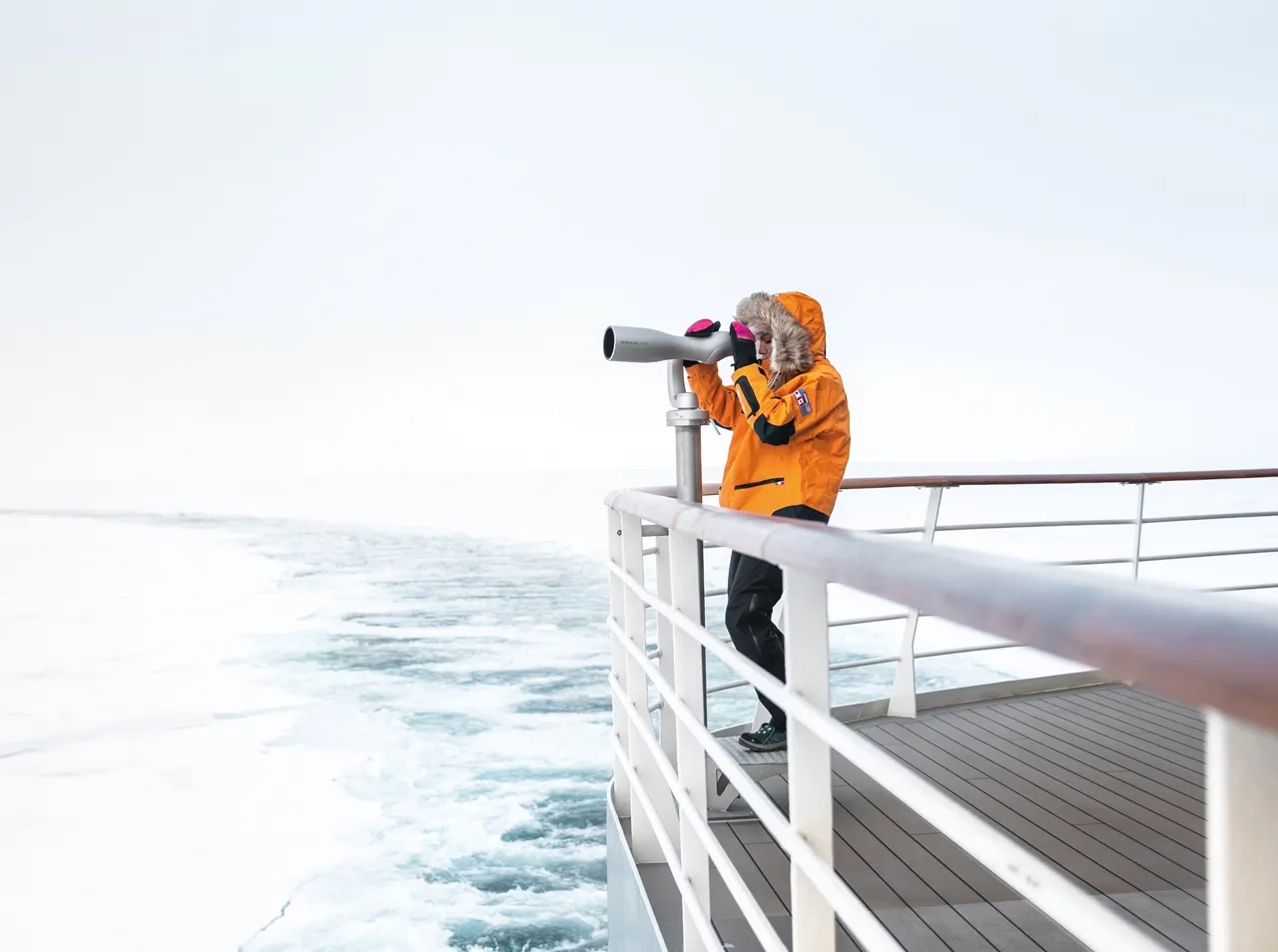 A man on the deck of an arctic cruise looking through a telescope 