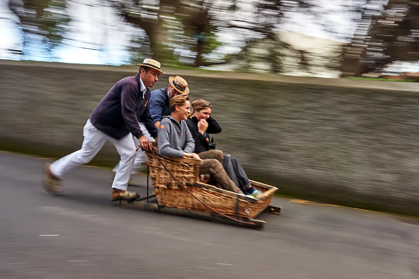 Traditional wicker toboggan ride with passengers being pushed down a paved street.
