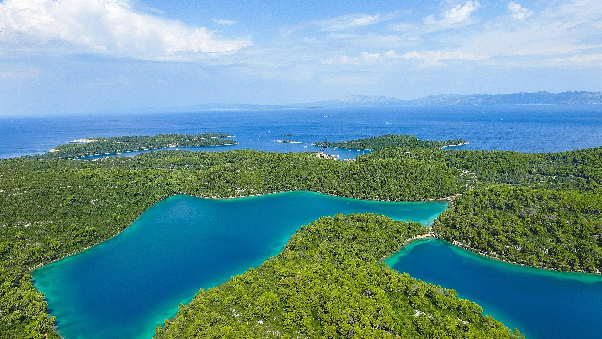 Aerial view of Mljet’s forested coastline with turquoise lagoons, small islands, and deep blue Adriatic waters.