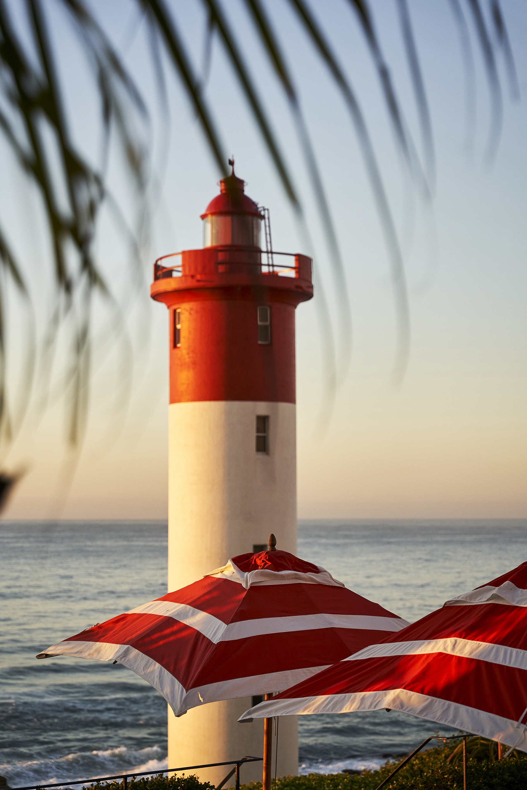 Red and white sun umbrellas set before a red and white lighthouse on the sea front