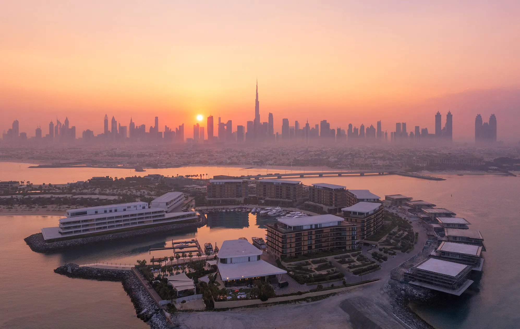 Aerial view of Bvlgari Resort Dubai at sunset with Burj Khalifa and city skyline in the background.