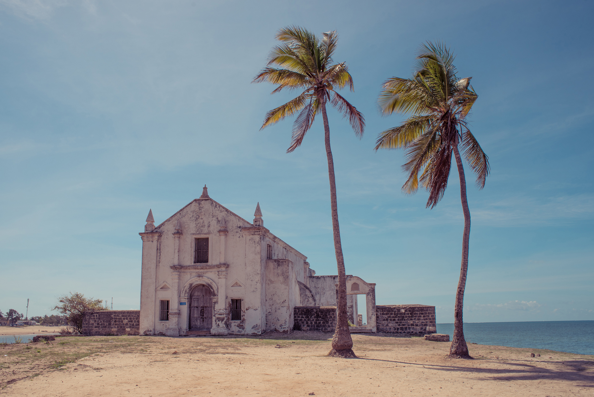 An old building on the beach with palm trees