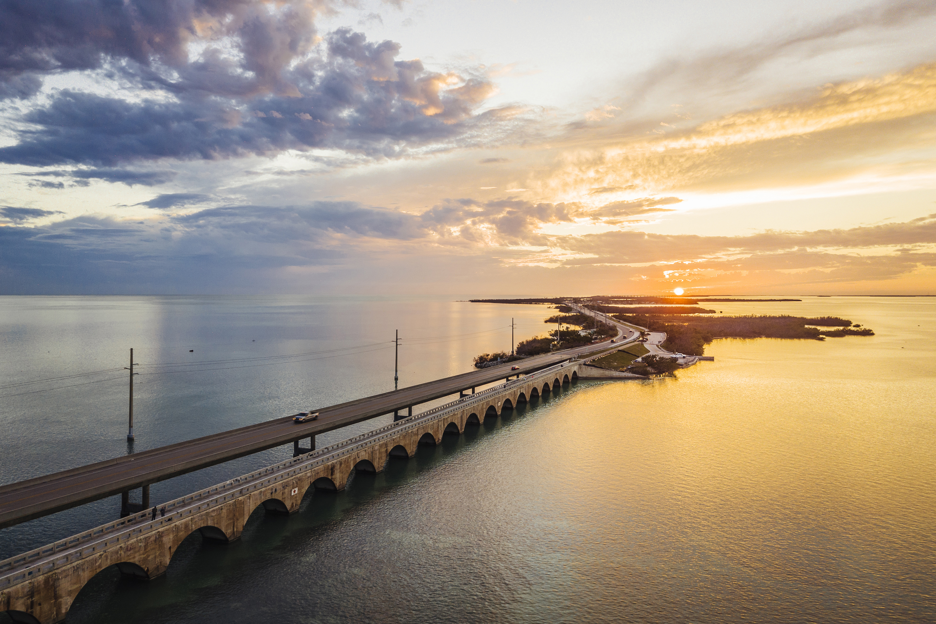 A long stretch of the Seven Mile Bridge in Florida crossing the ocean onto an islet with the sun setting on the horizon