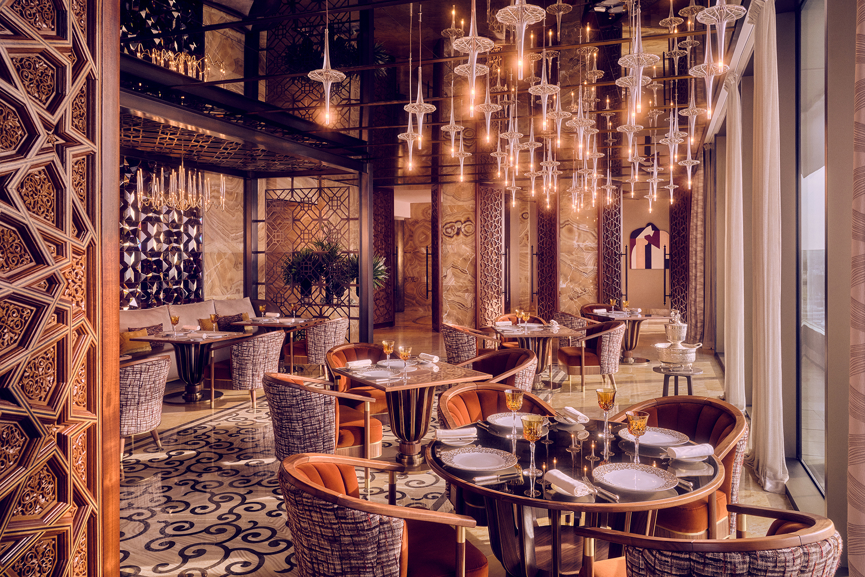 The ornate interior of a restaurant at Royal Mansour Casablanca featuring a statement light fixture, patterned room dividers and plush furniture