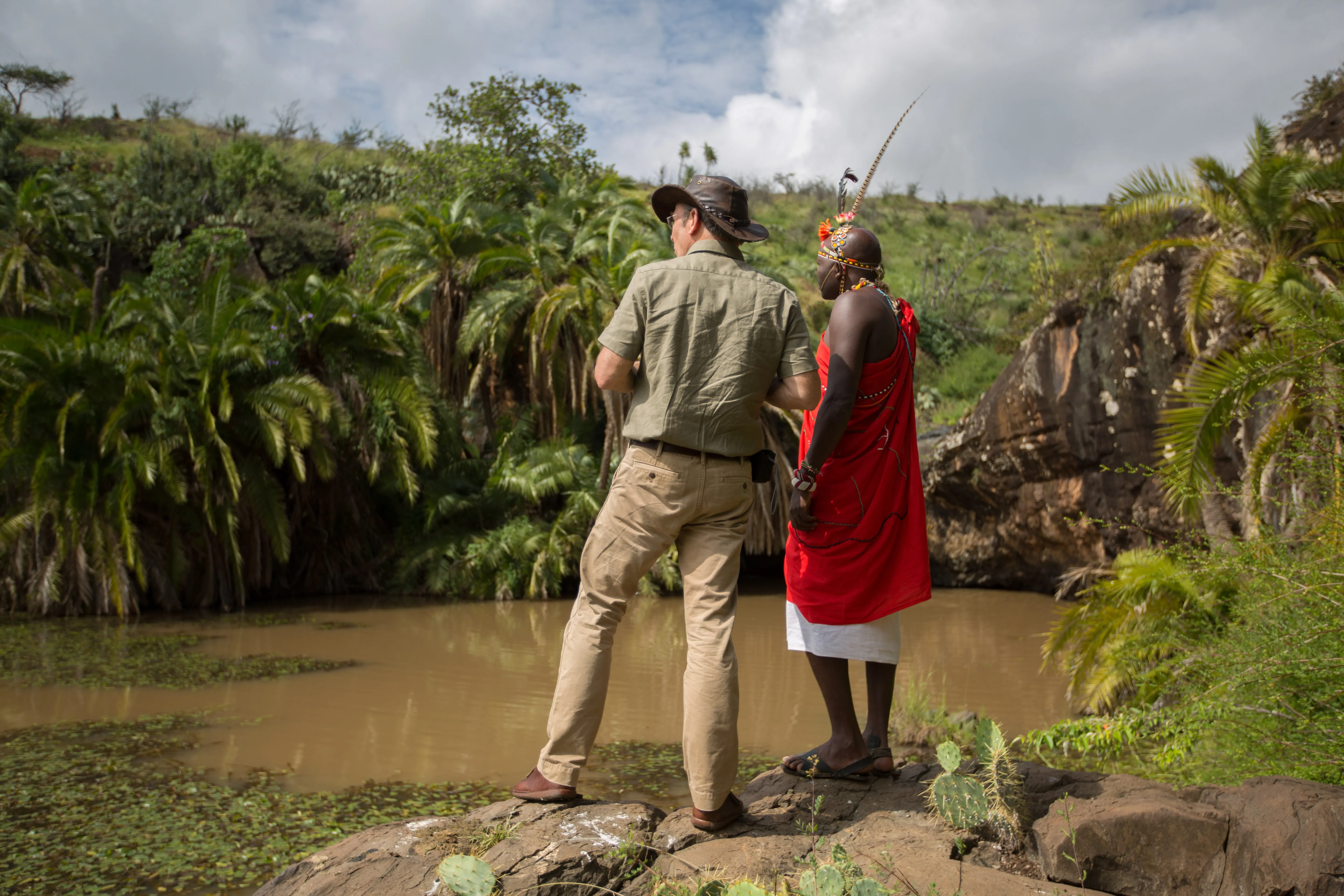 Two people stood beside a waterhole at Elewana Loisaba Tented Camp surrounded by green plants