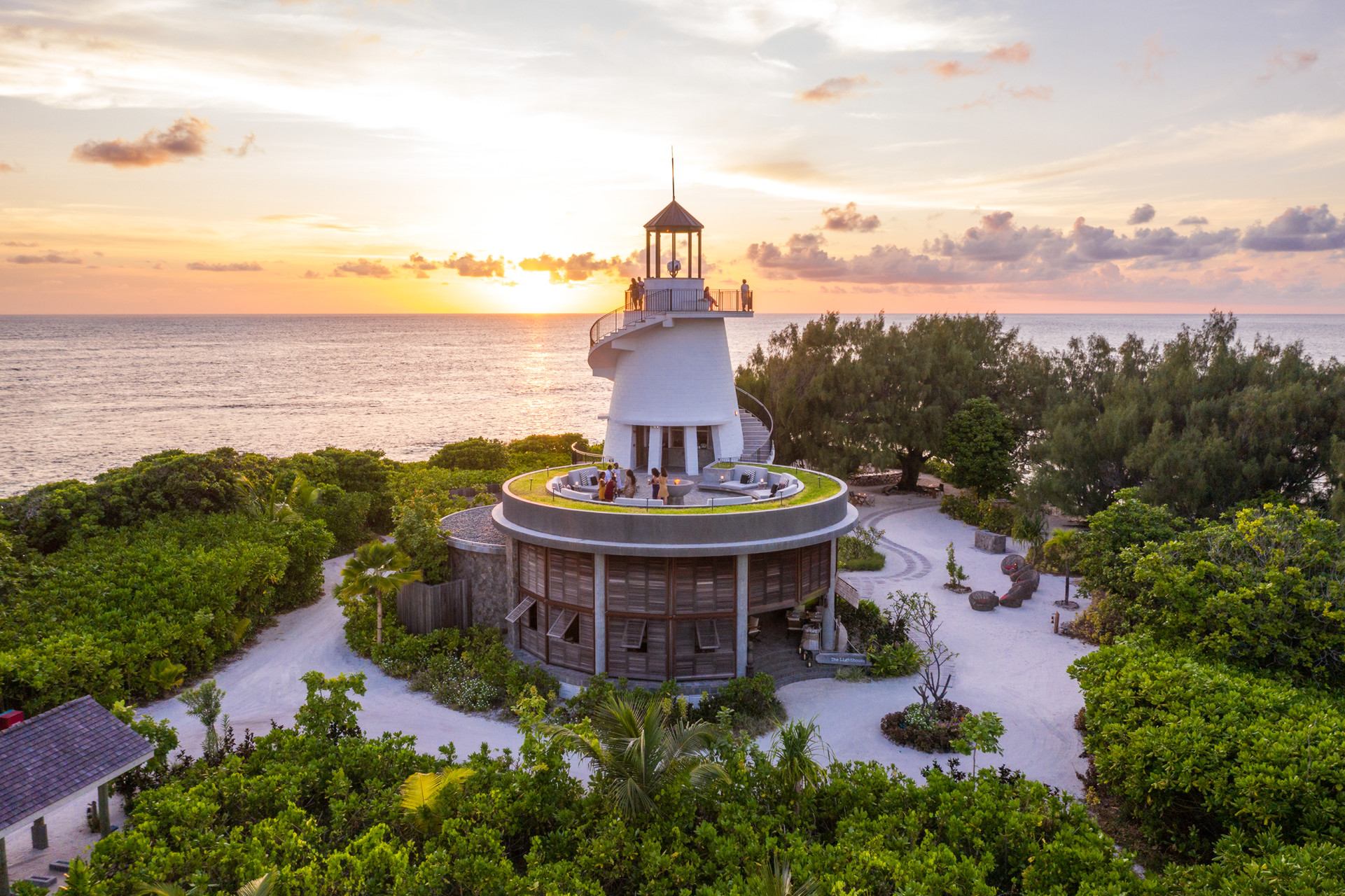 A tall lighthouse-style building surrounded by greenery with the sunset behind at Four Seasons Resort Desroches Island