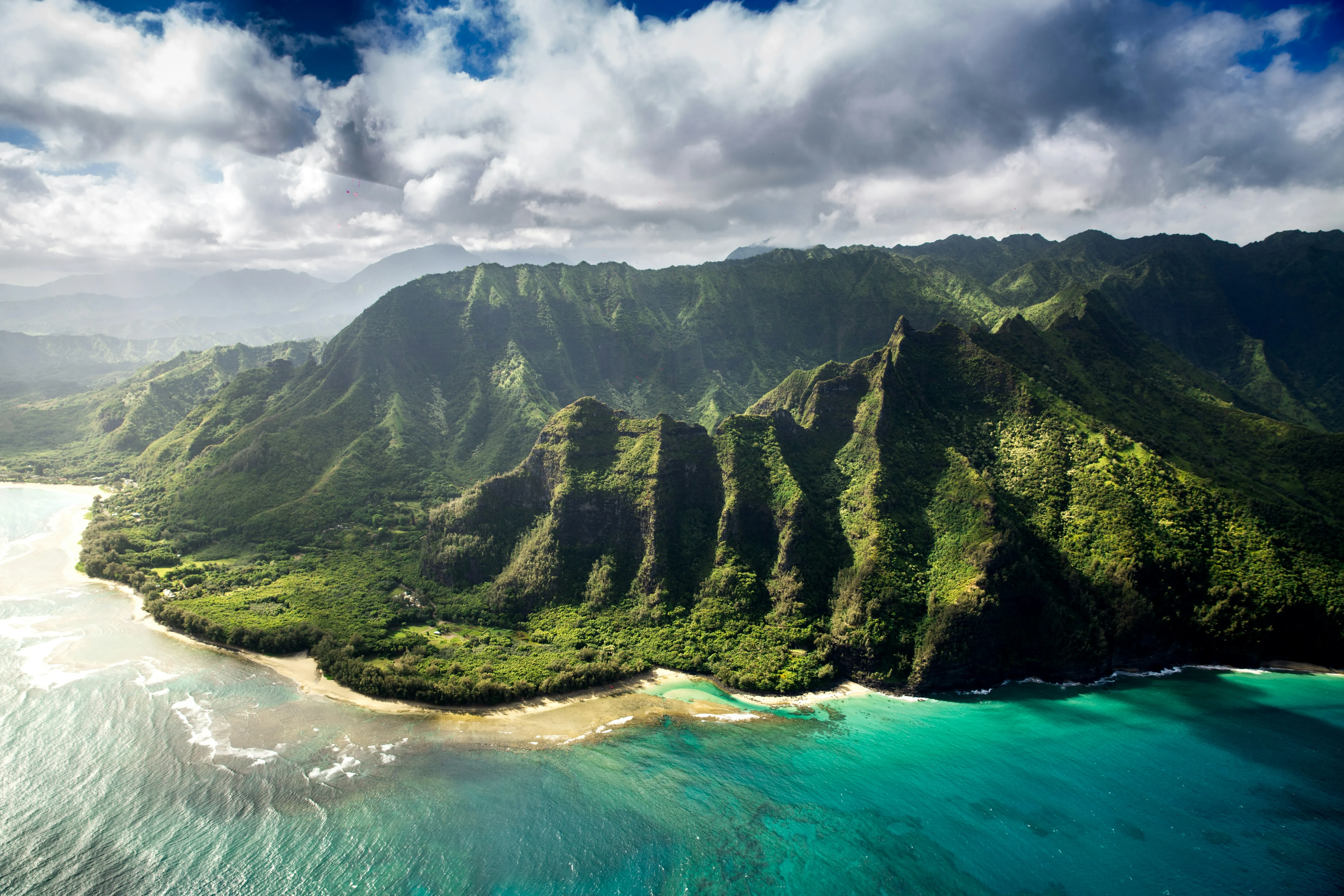 The large green mountains of the Island of Hawaii with a clear sky overhead and turquoise ocean beneath