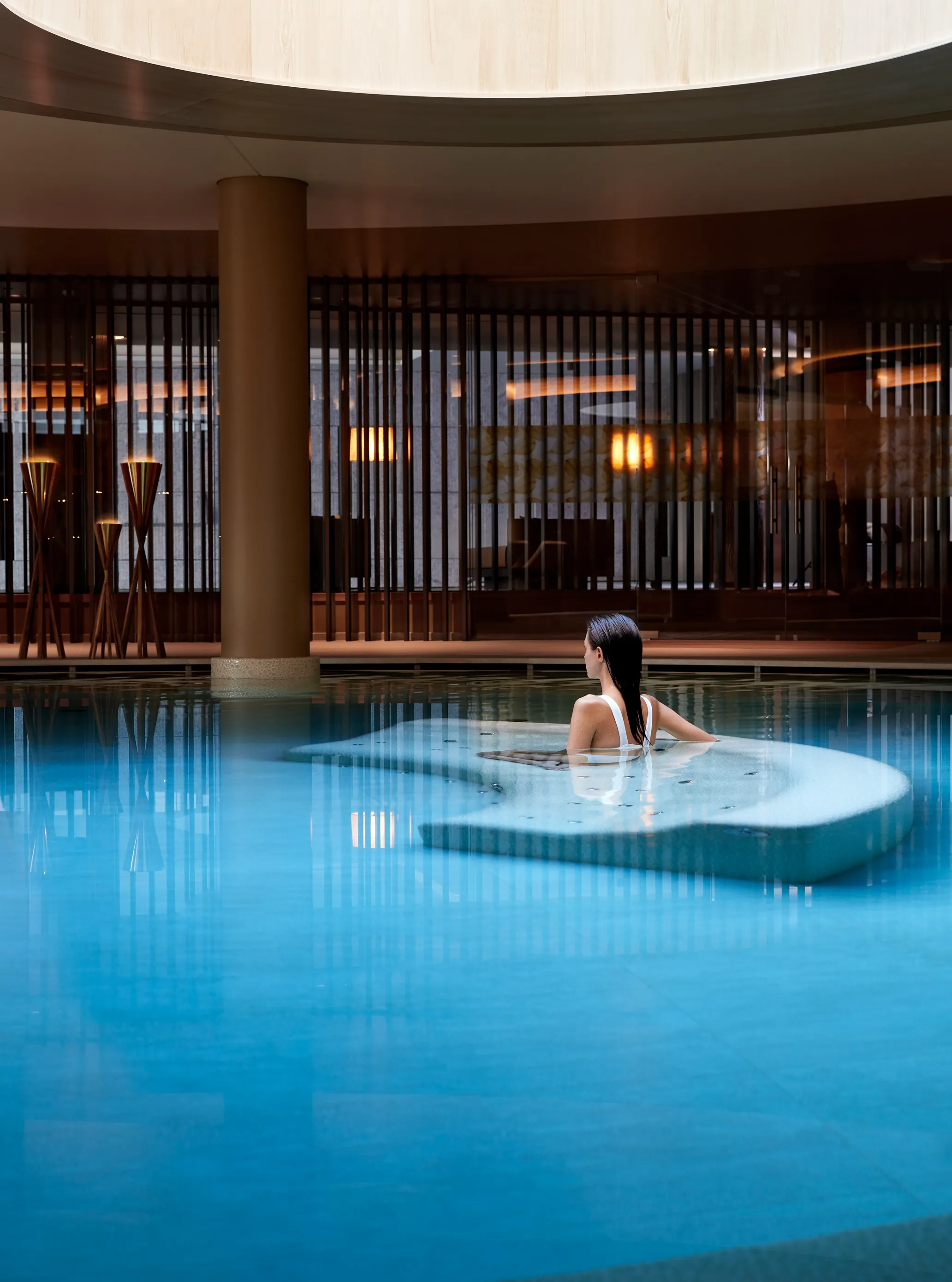 Woman relaxing in a tranquil indoor hydrotherapy pool with submerged loungers.
