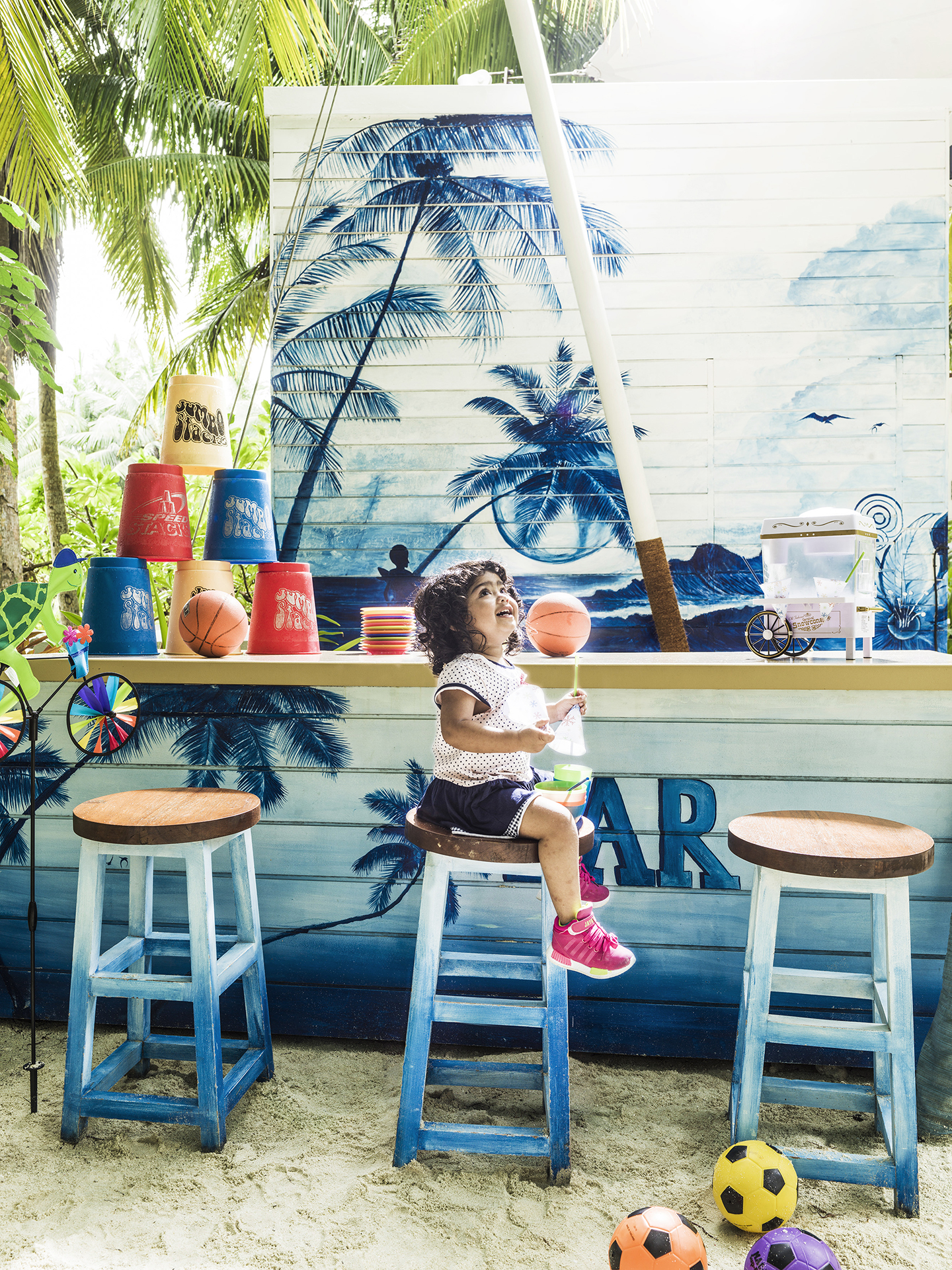 A young girl sat on a stool at an ice cream bar at One&Only Reethi Rah