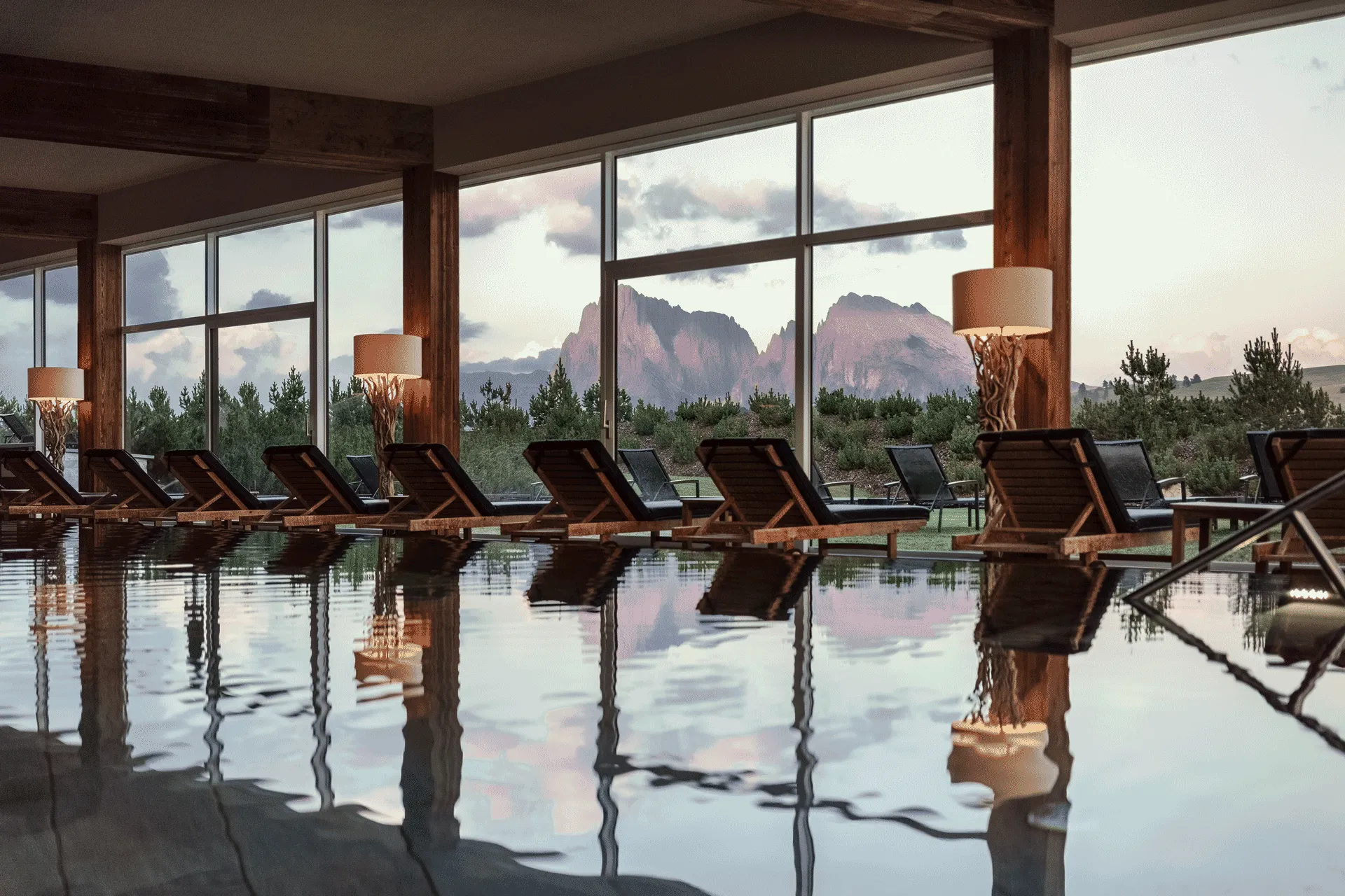 Indoor pool at COMO Alpina Dolomites with loungers and panoramic mountain views through floor-to-ceiling windows.
