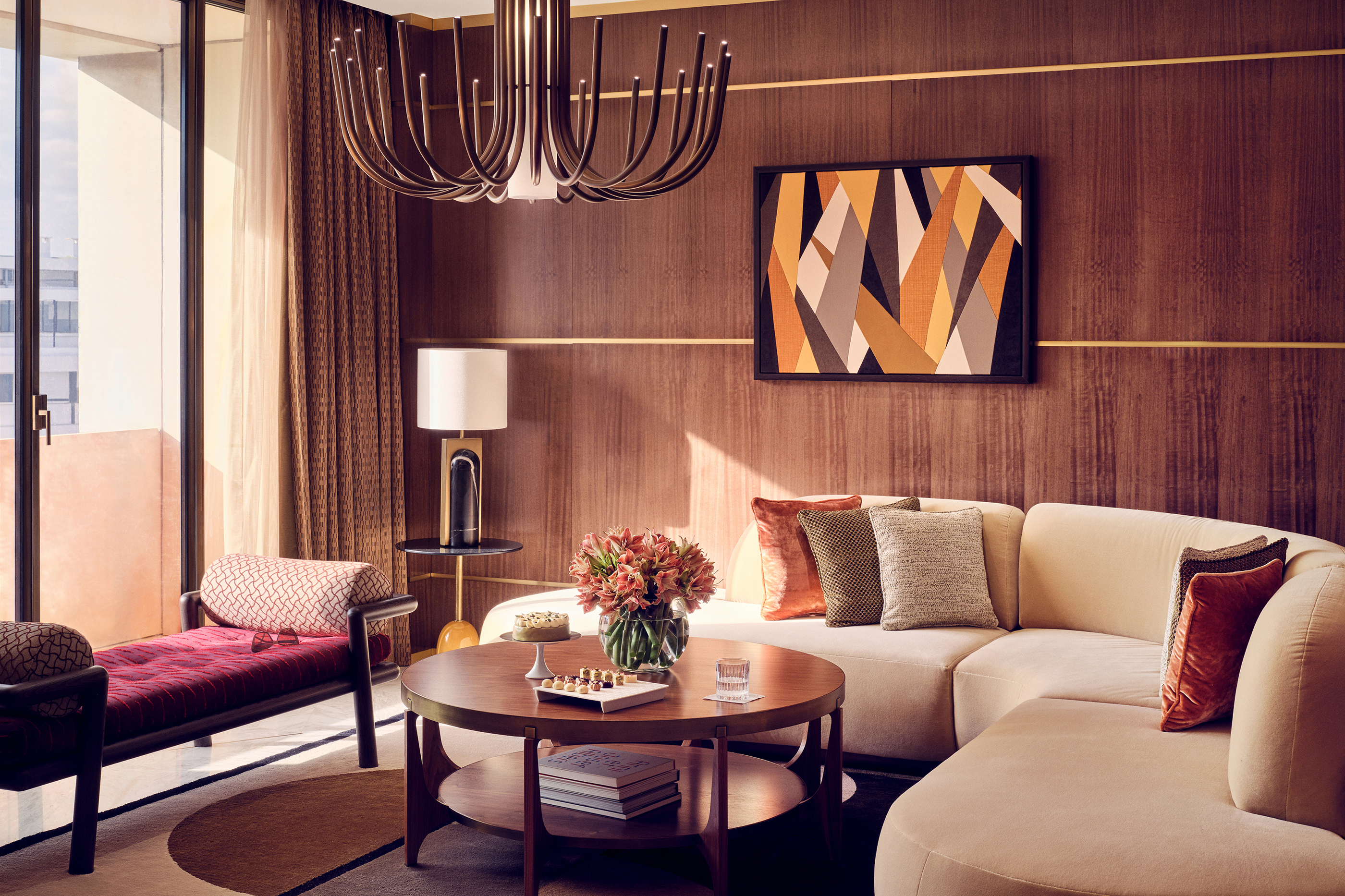 A seating area of a suite at Royal Mansour Casablanca featuring a plush sofa with cushions, a coffee table and statement chandelier with artwork on the wall behind