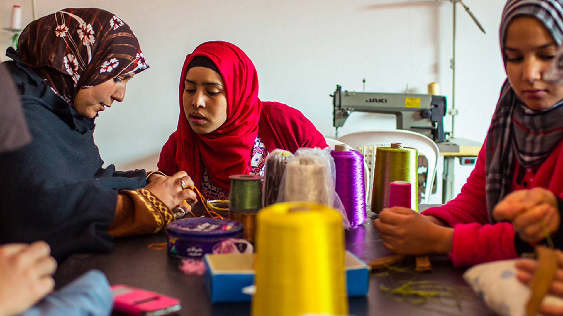 Three women in colourful hijabs sat at a table with sewing equipment