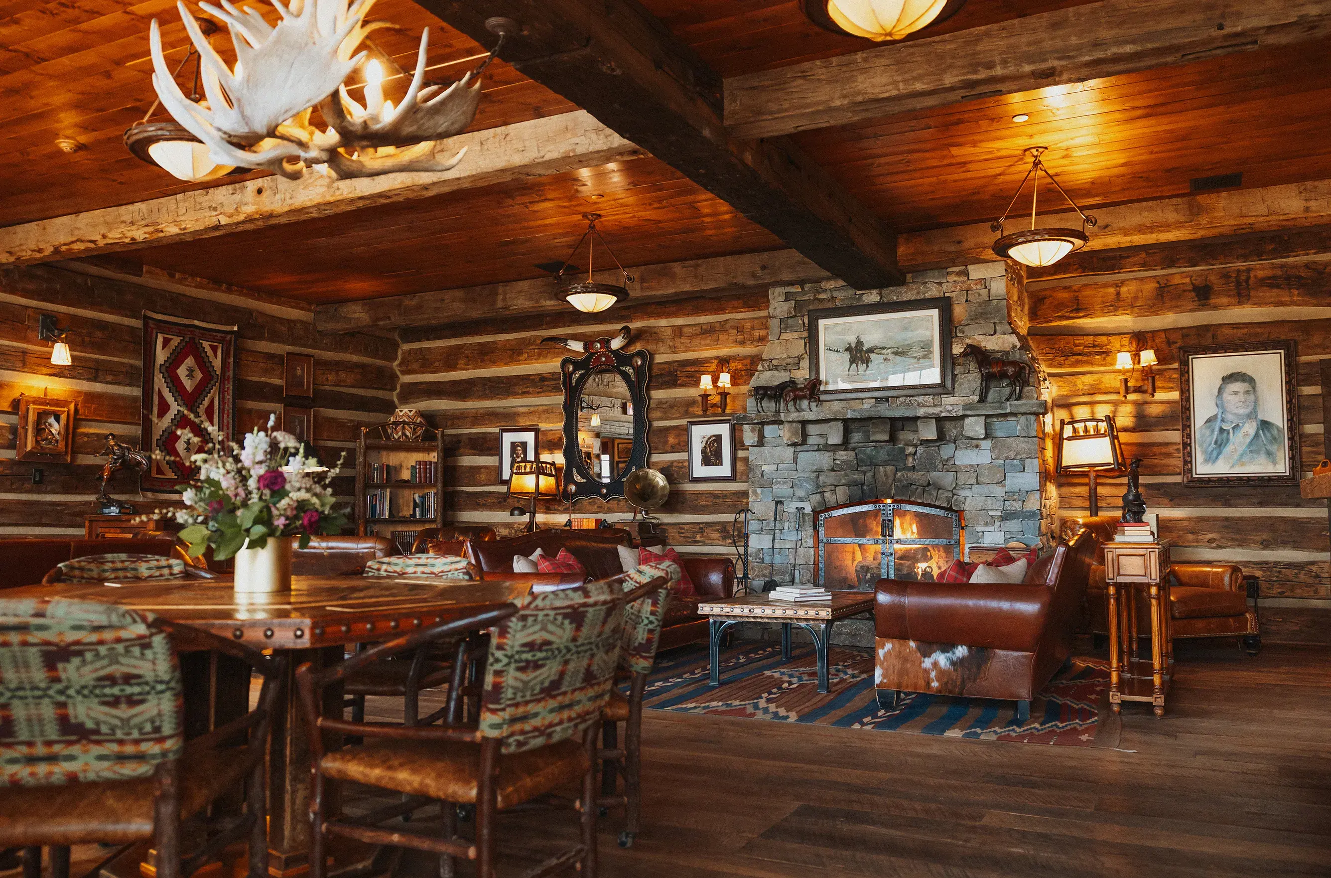 Cosy lounge at The Ranch at Rock Creek in Montana featuring rustic ranch-style furniture set in front of a stone fireplace within log walls adorned with western pictures and artwork