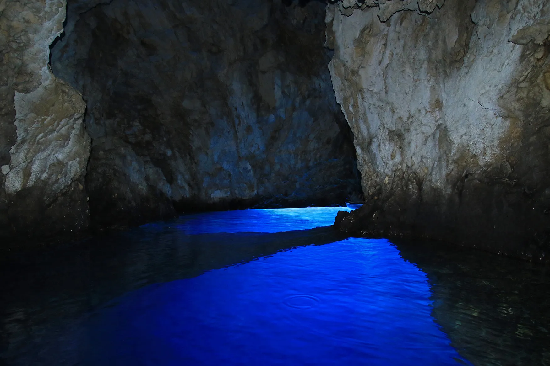 Sea cave with glowing blue water reflecting against rocky walls.