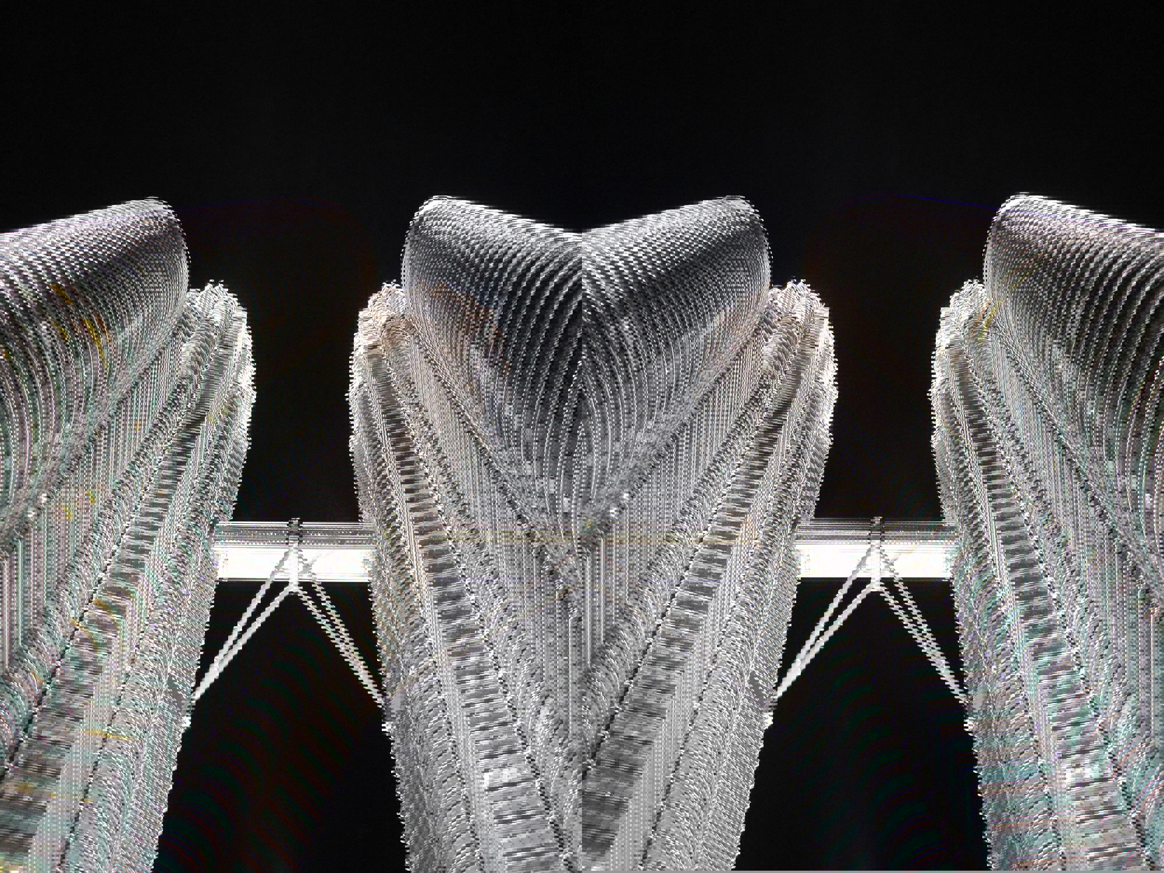 A ground view of the petronas towers and skybridge in Kuala Lumpur lit up at night and soaring into a black sky