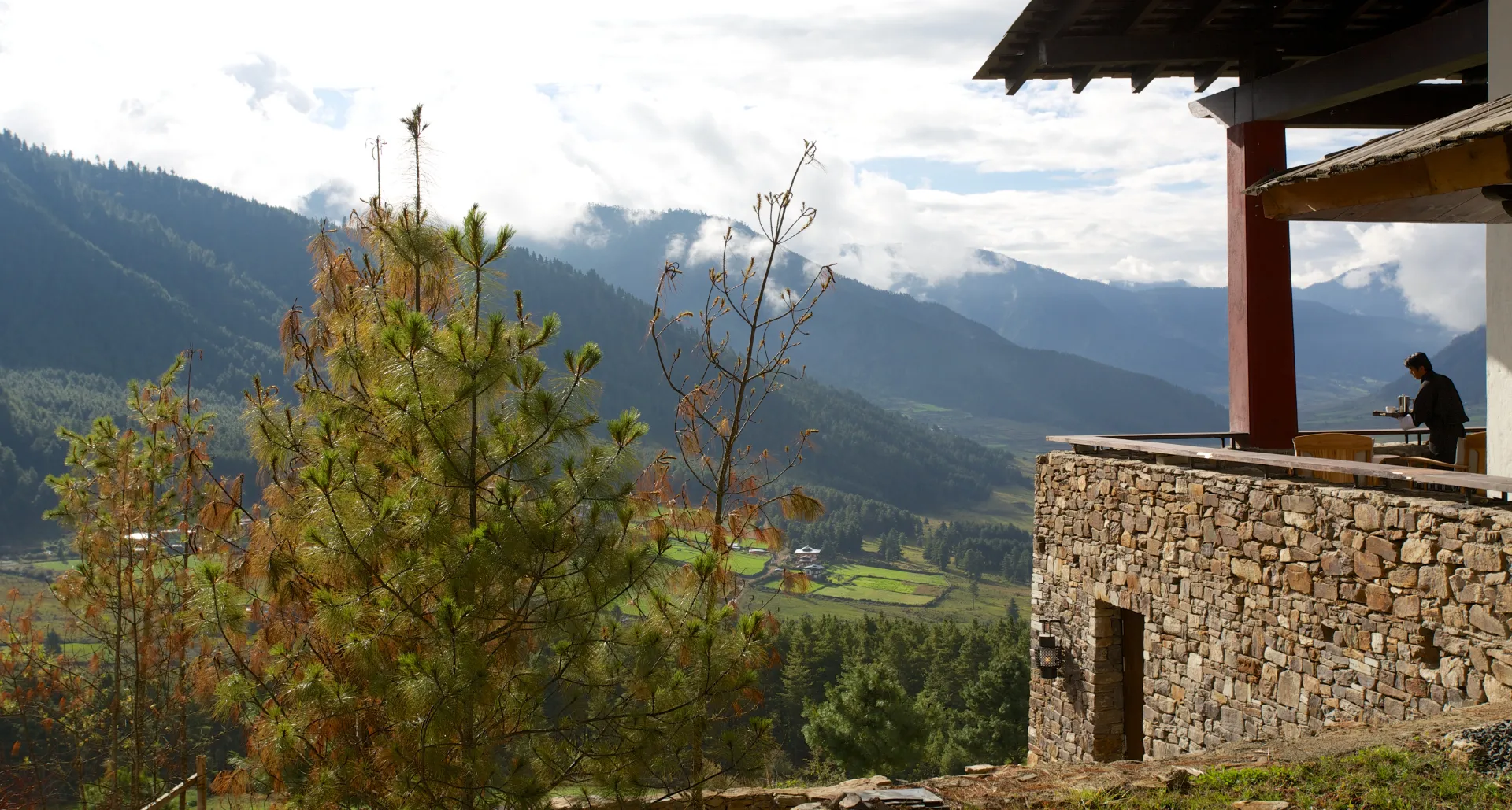 Stone lodge terrace set above a scenic valley with sweeping views of forested hills.