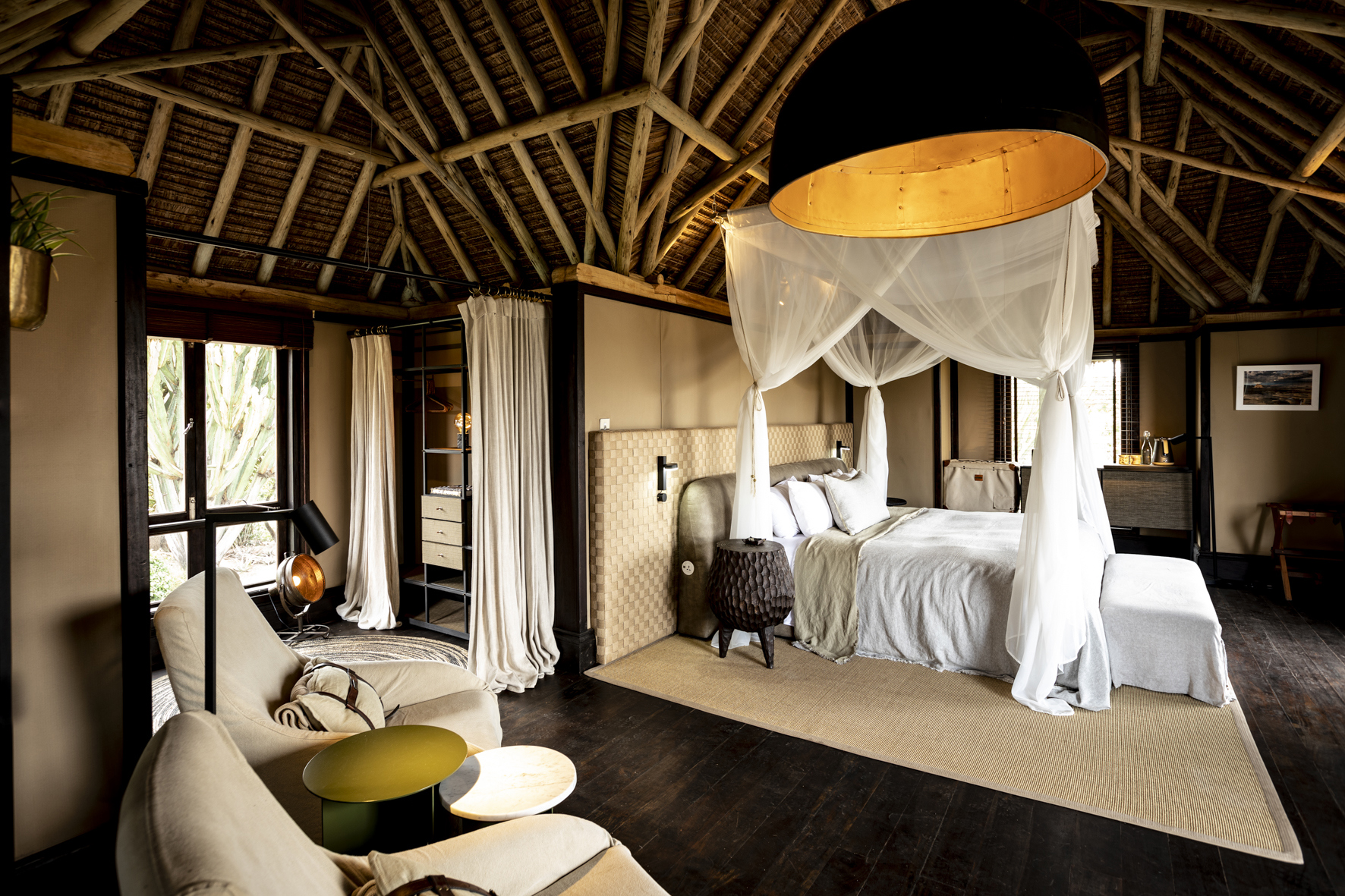 A large vaulted bedroom with four posted bed and comfy sofas with large wardrobe area behind curtains