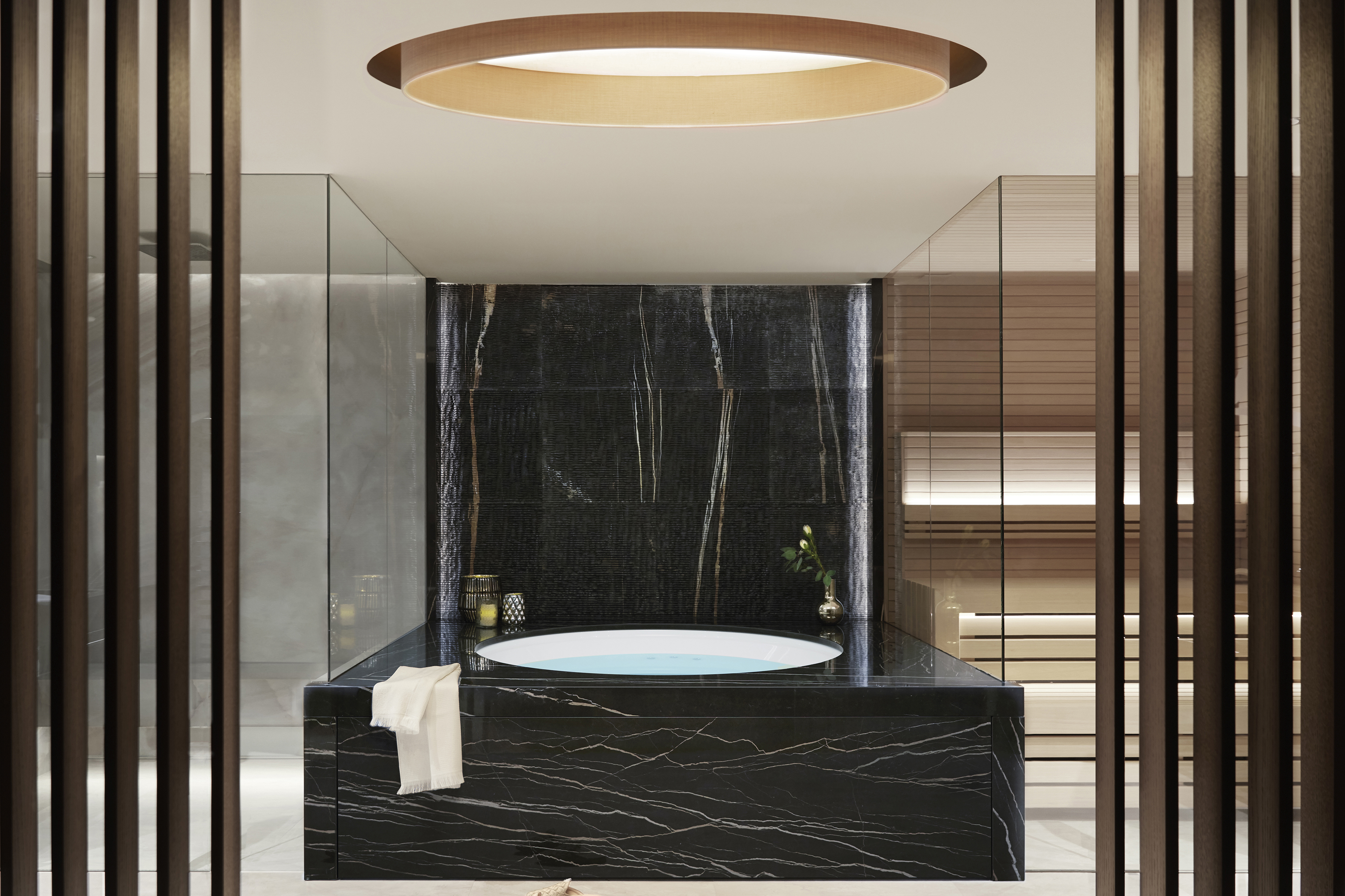 Exclusive spa suite bathroom with large circular black marble bathrub and circular ceiling window above 