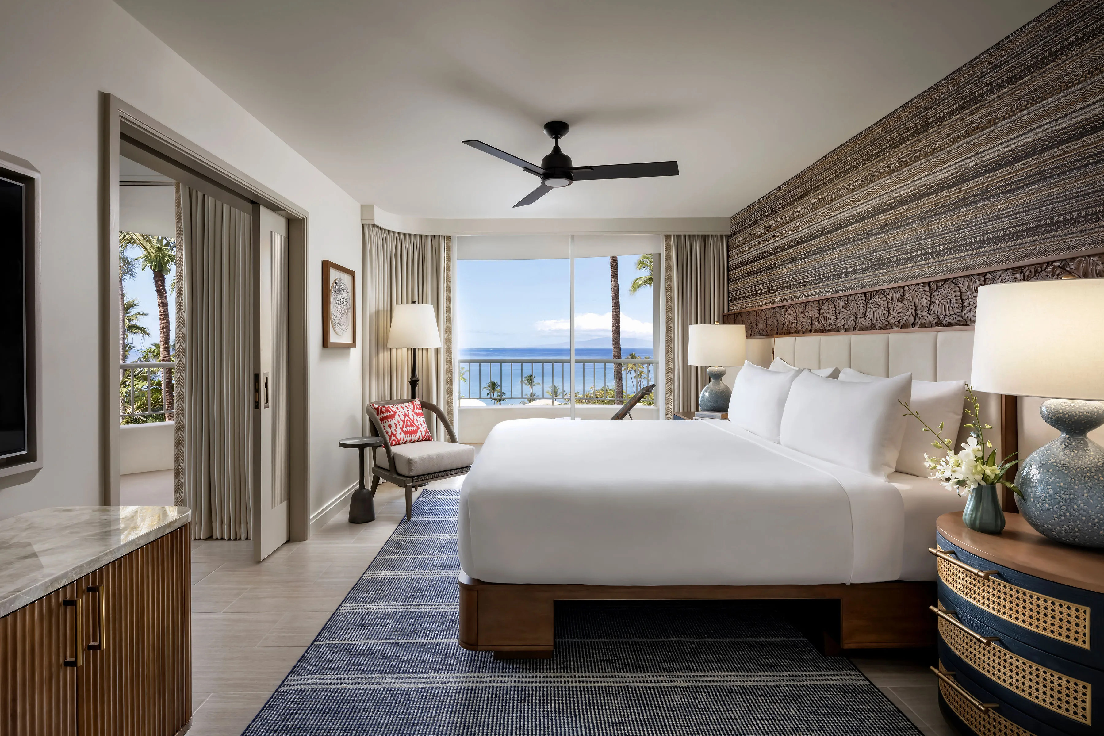 Bedroom of a Kea Suite at Fairmont Kea Lani featuring pale furnishings and Hawaiian-inspired decor, with large sliding doors leading out and a view of the ocean
