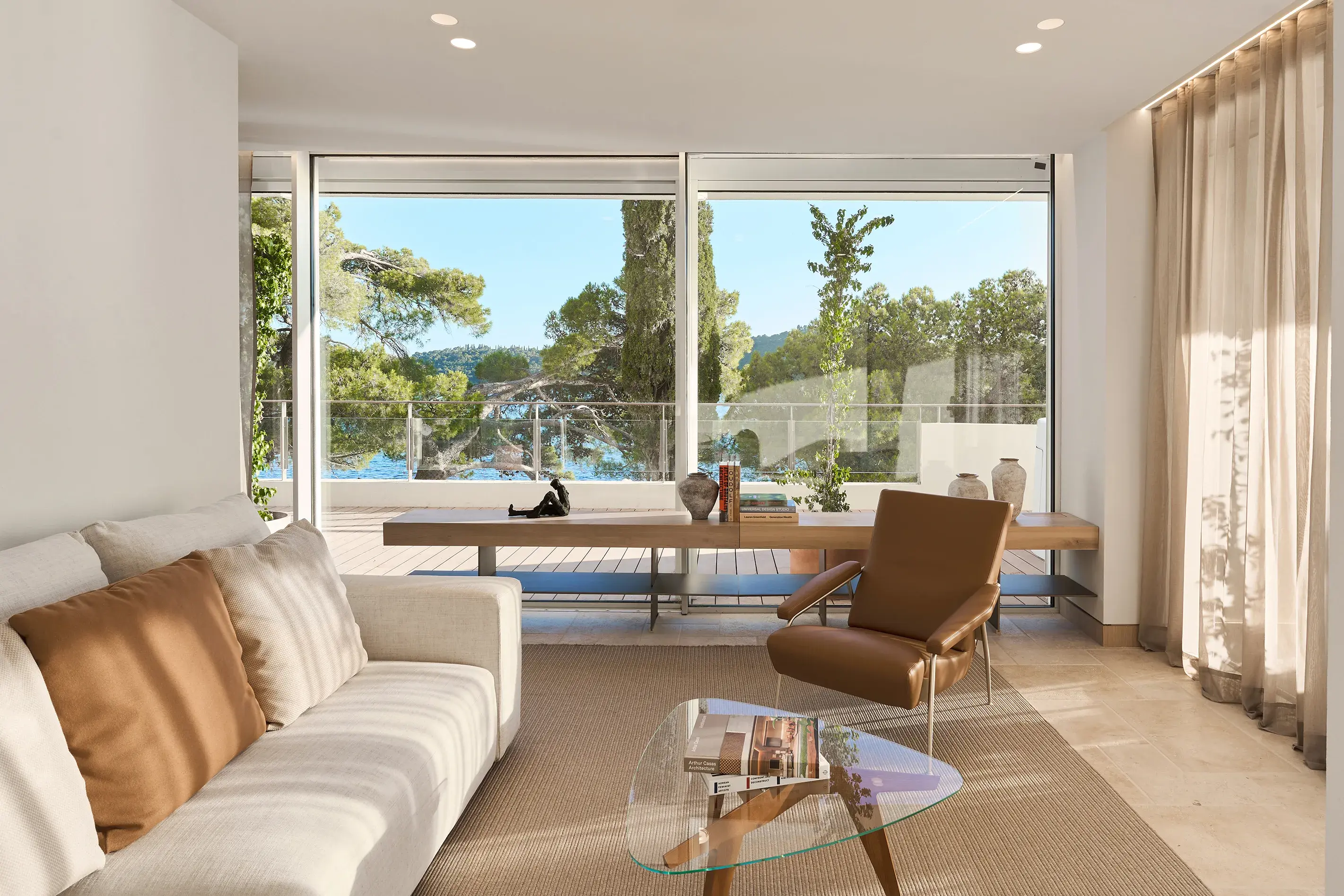 Living room of Tezoro Suite at Villa Dubrovnik in Croatia featuring stylish mid-century modern furniture and wrap around windows with curtains and a view of the sea and greenery outside