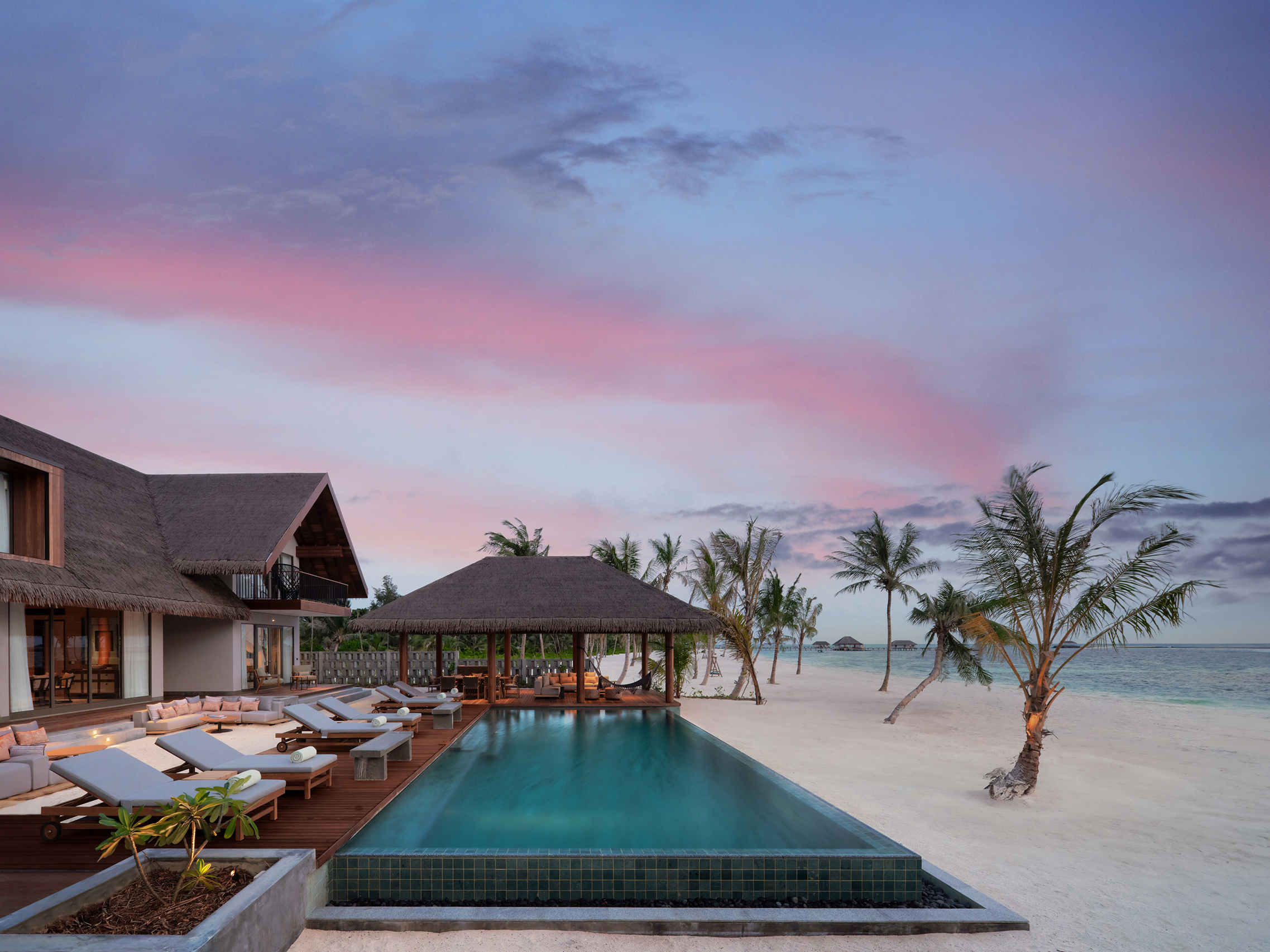 Beach reserve pool lined with loungers fronting the beach at sunset at Six Senses Kanuhura