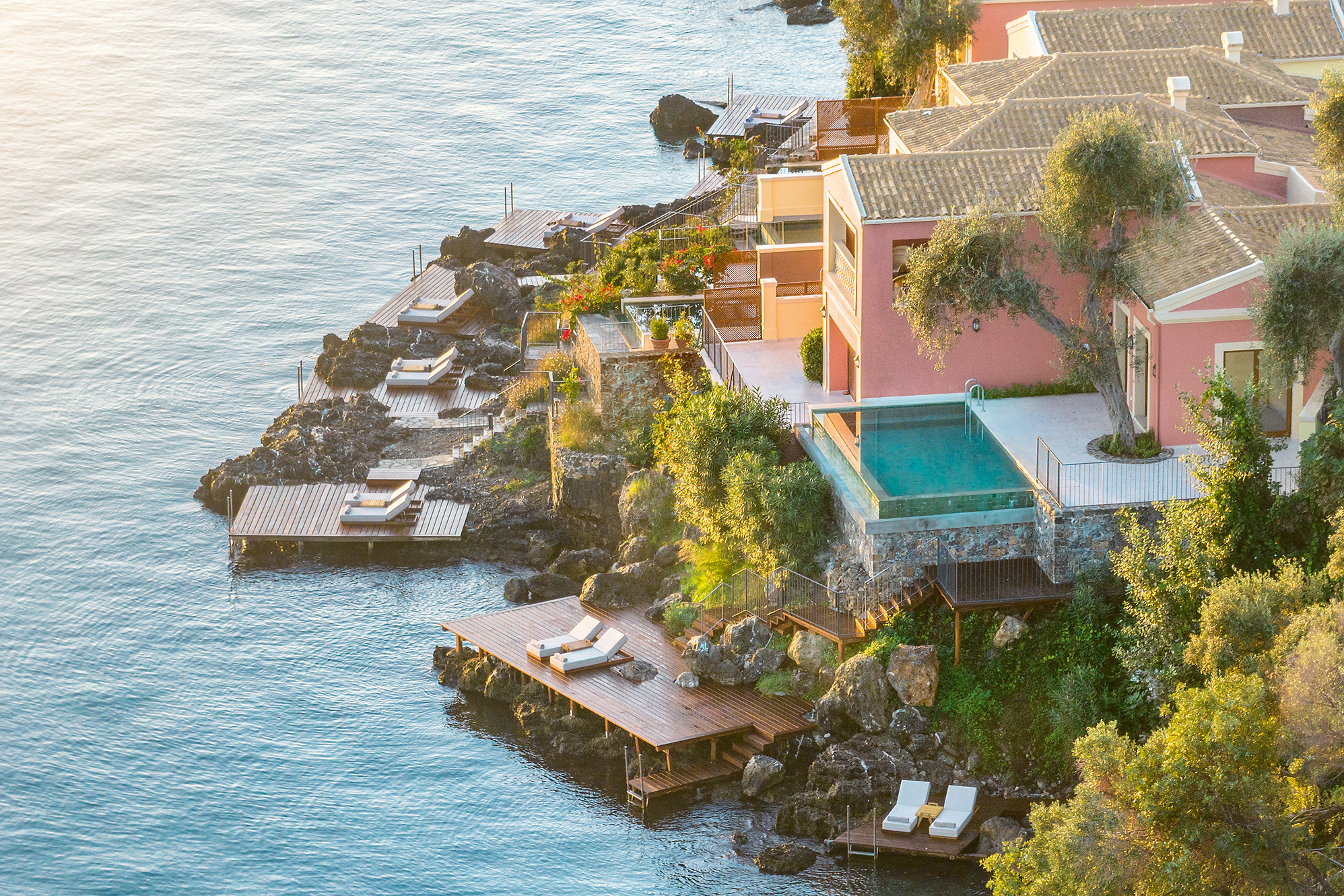 Aerial view of Palazzo Odyssia seaside villas with private pools at Grecotel Corfu Imperial, nestled in lush greenery by the Ionian Sea.