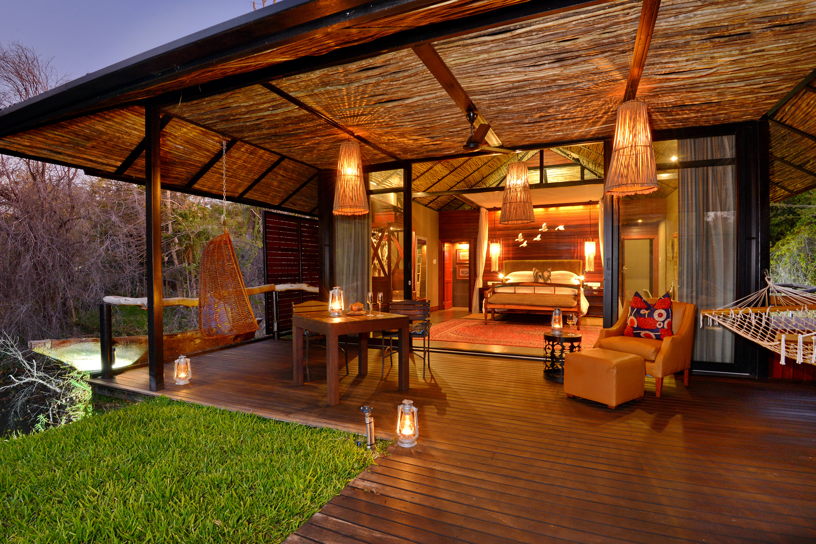 A luxurious lodge room at Mukwa River Lodge with an open wooden deck, dining table, hammock, cozy seating area, and warm lantern lighting.