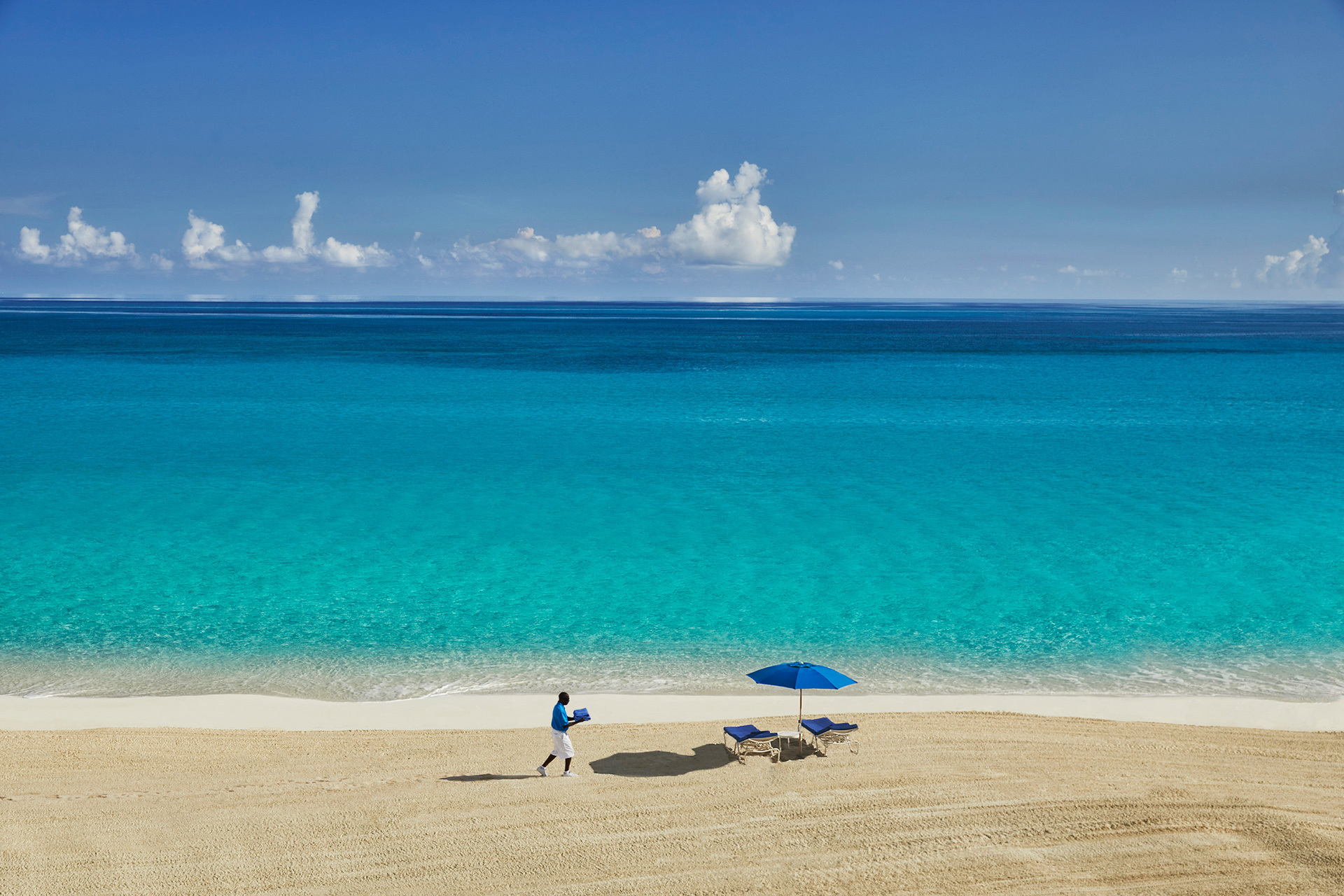 A man on a beach carrying towels to some sun loungers