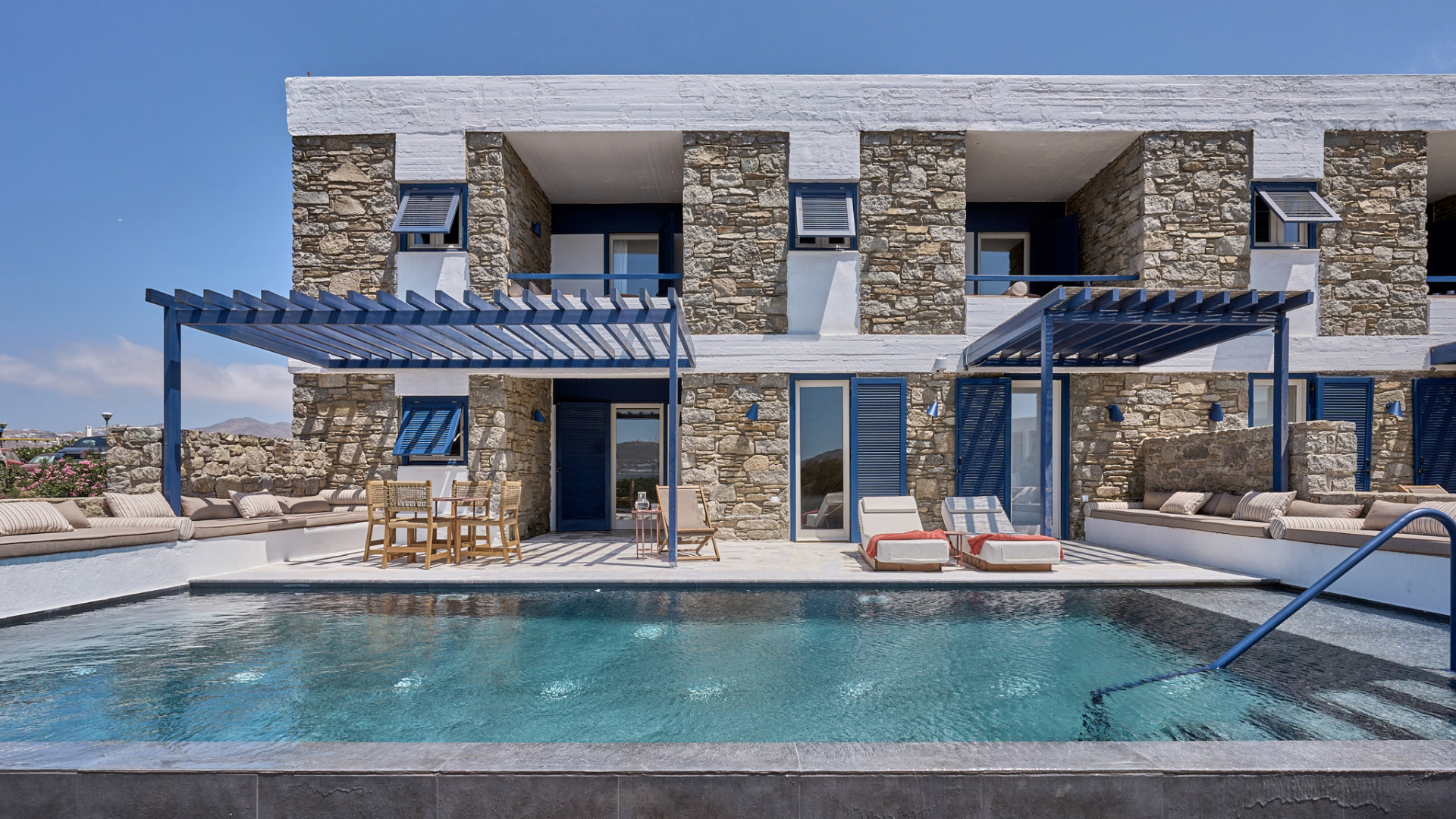 A stone building with a pale terrace leading to a large private pool