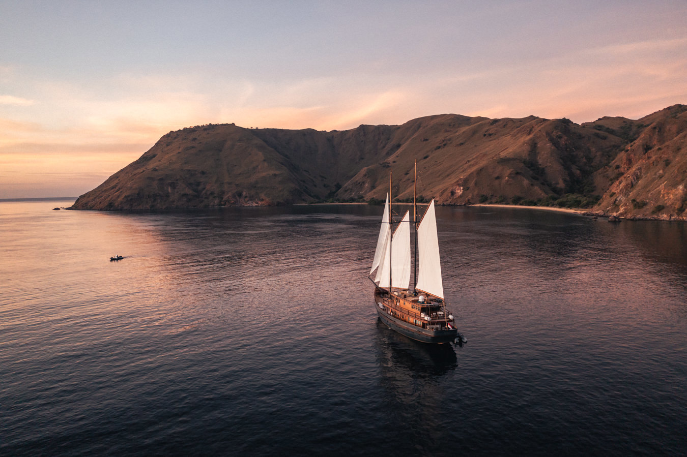 The Vela yacht sailing across a still ocean with an island behind