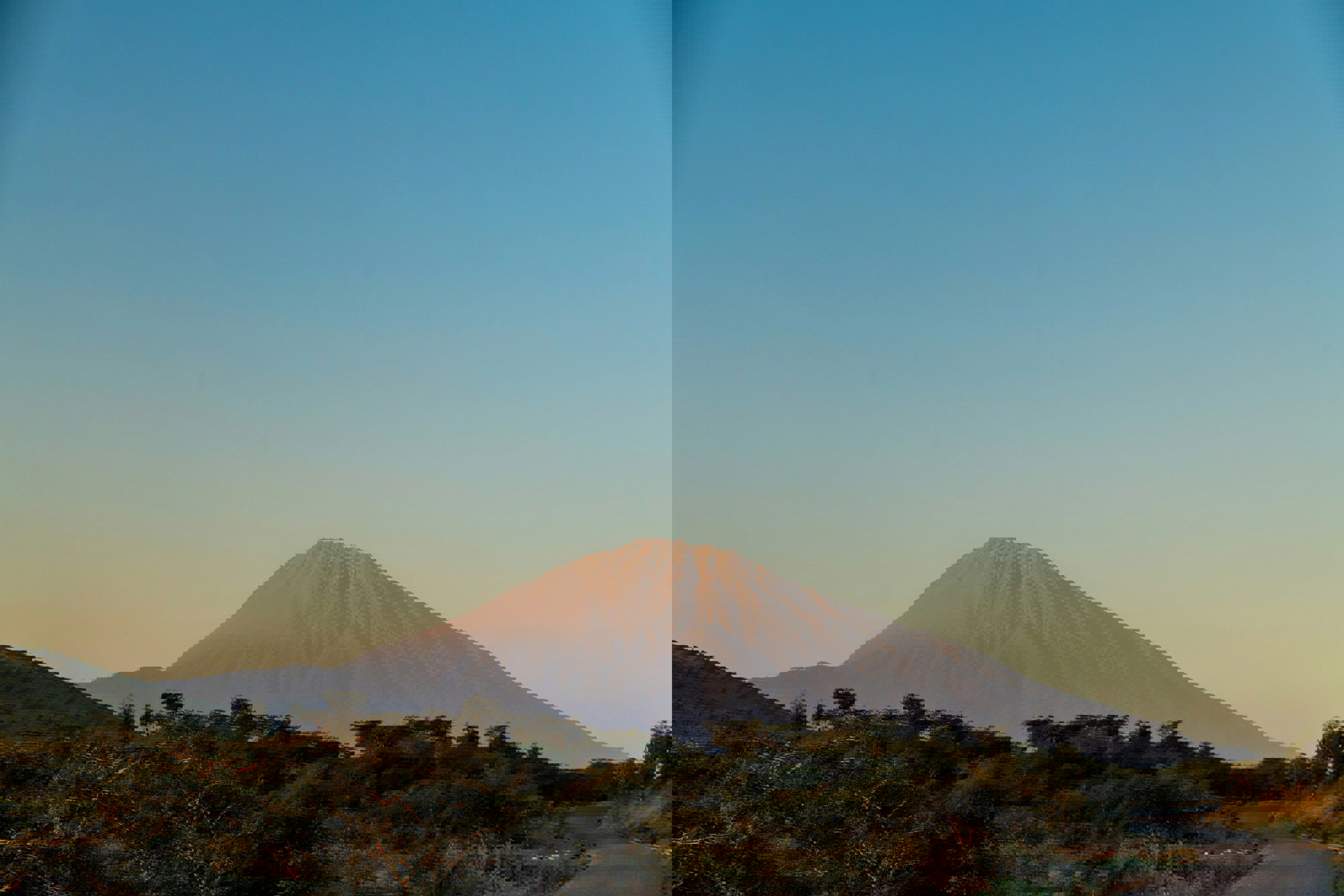 Mount Meru in Arusha, Tanzania under a clear sky with forests and a glimpse of a road in the foreground